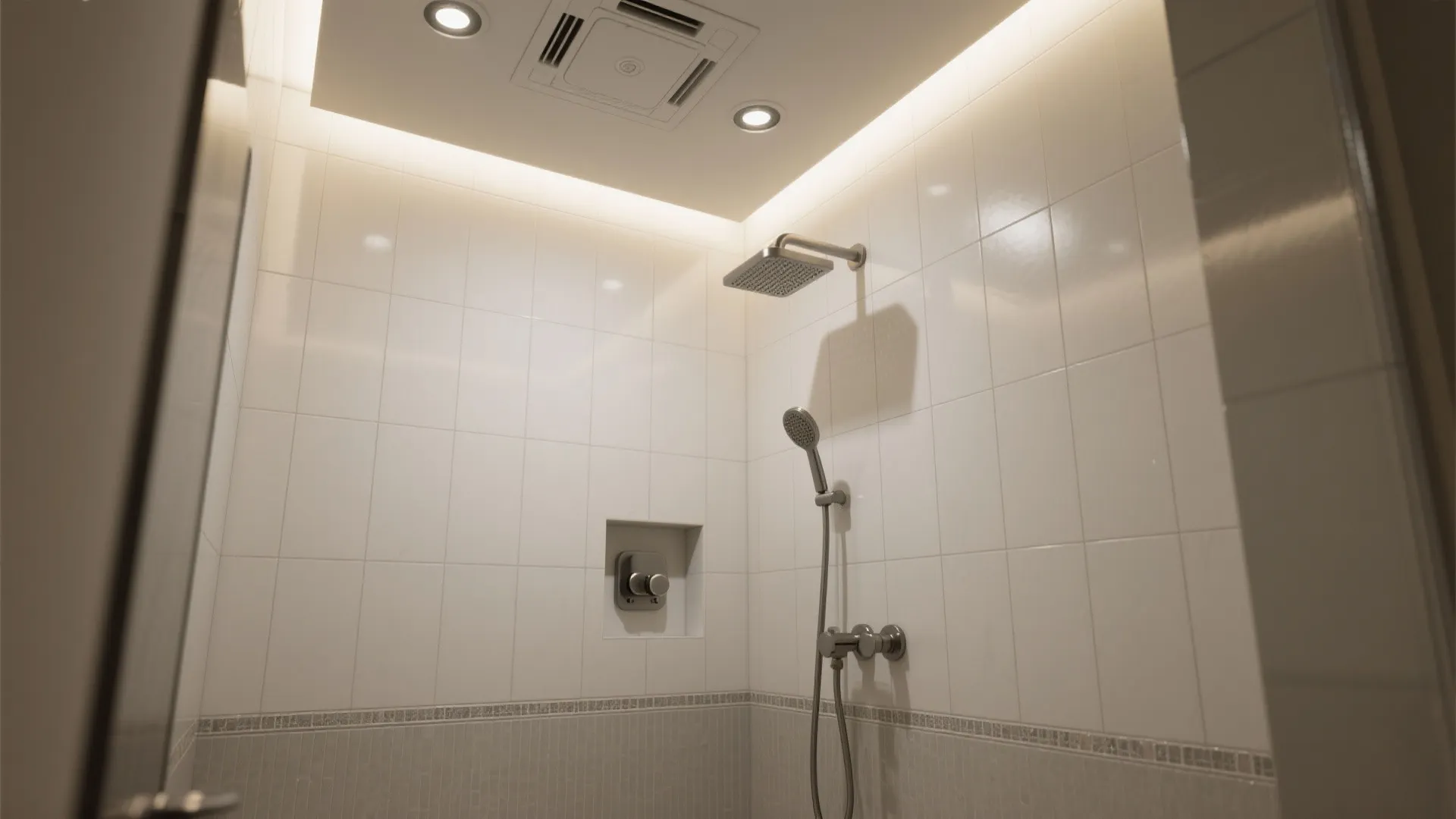 Clean white tiled shower room with silver shower head wall controls and bright recessed ceiling lights