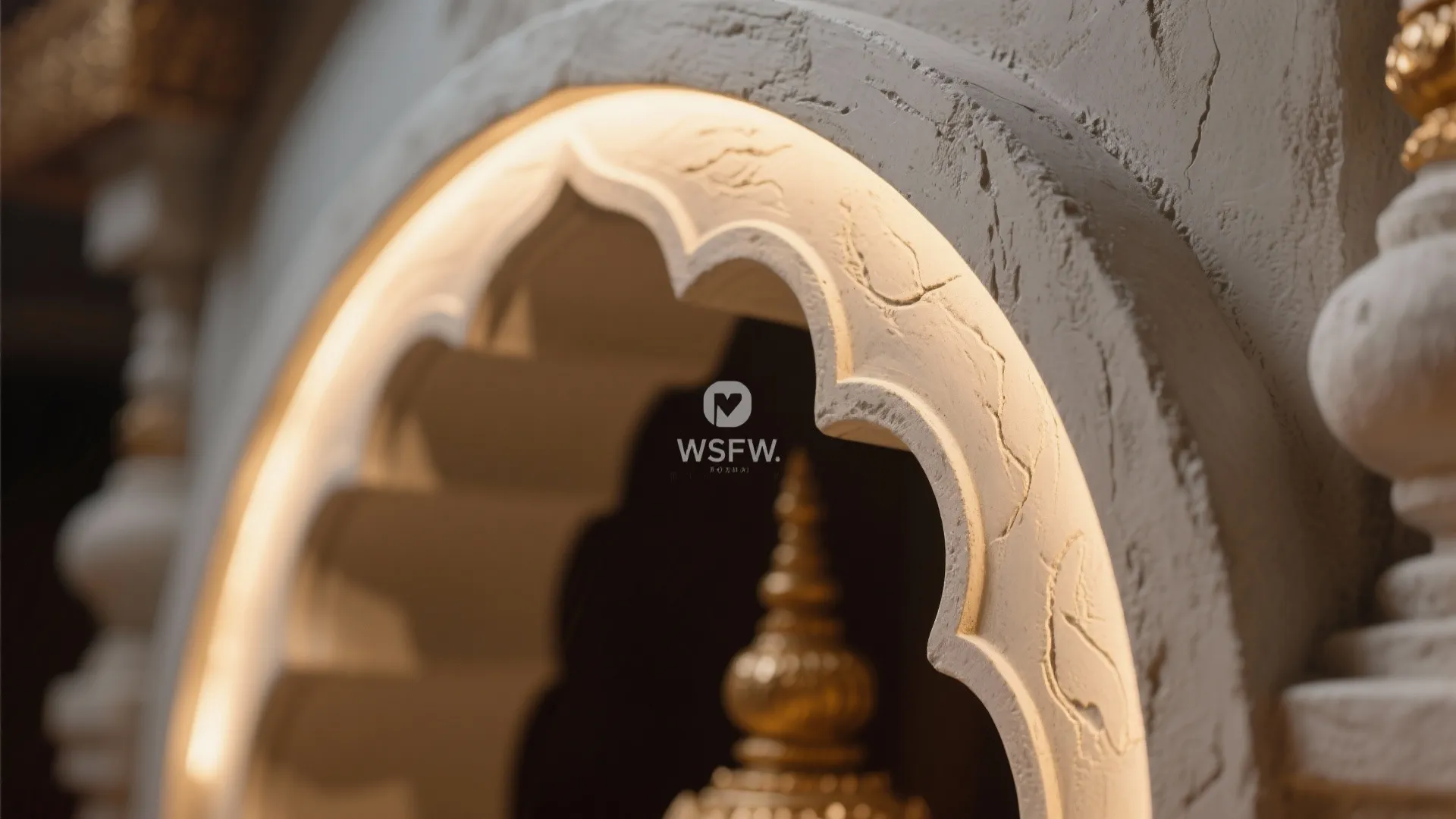 White textured stone wall arch with built in yellow lights and a golden statue top