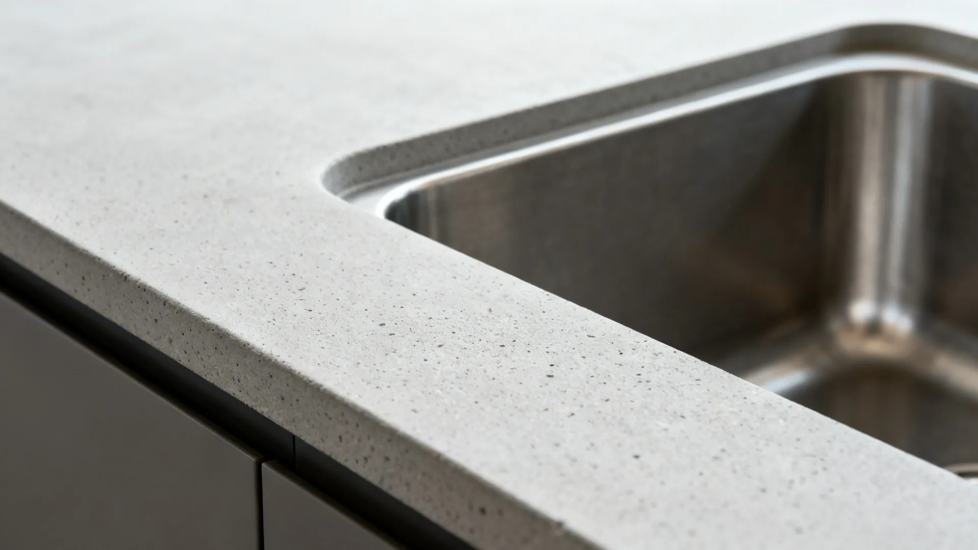 Macro of light gray countertop with an integral drainboard near a sink.