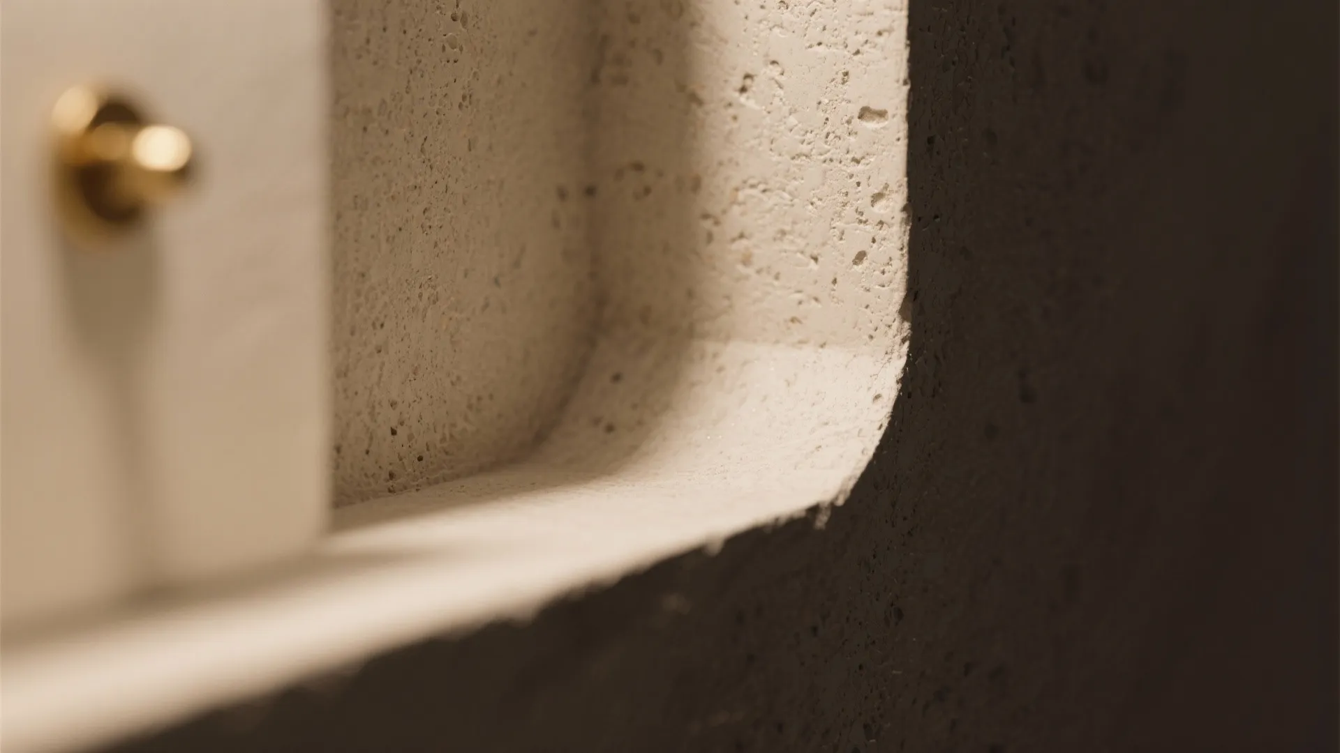 Close up view of textured light grey wall corner with small gold metal wall hook