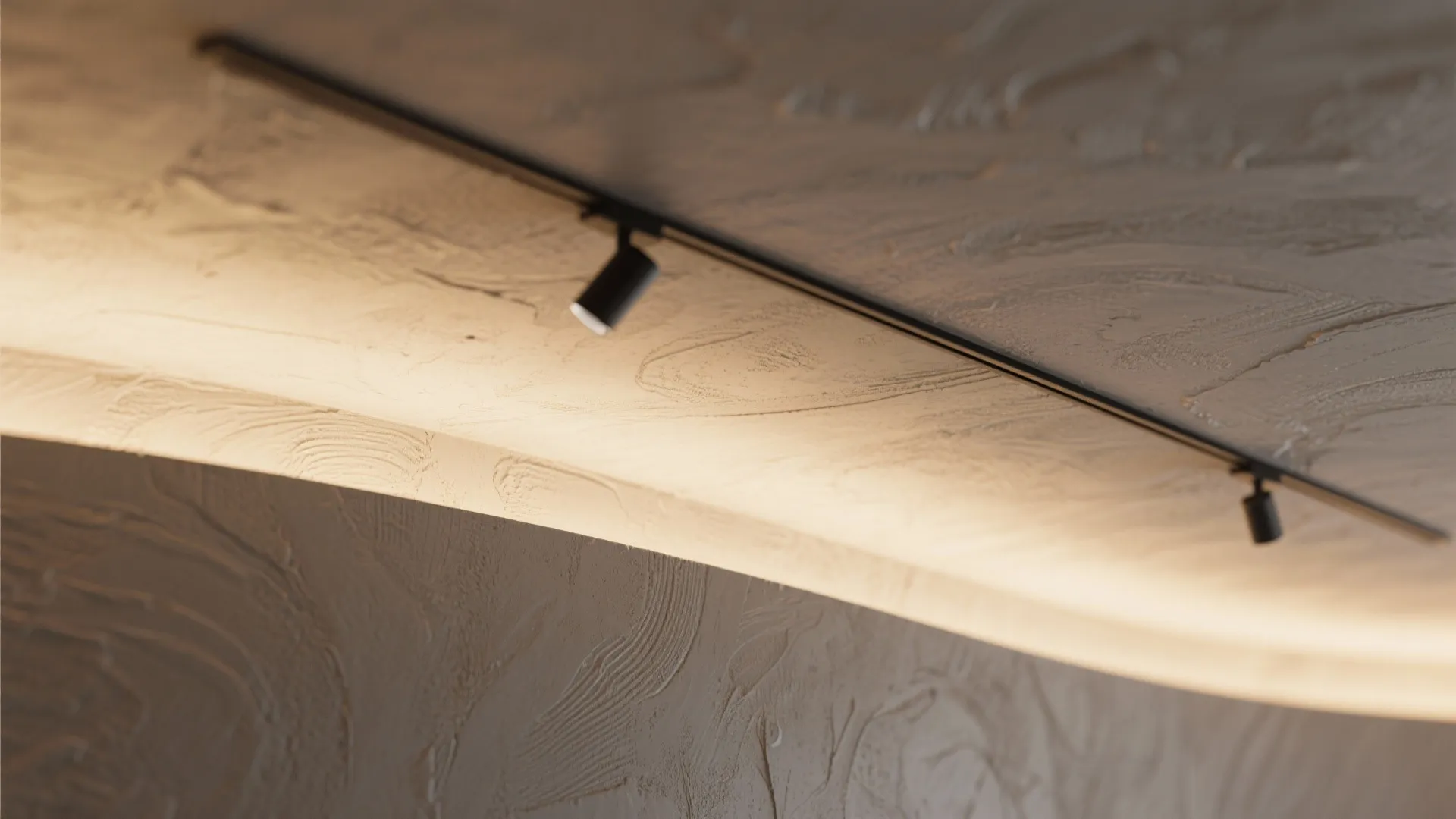 Close up of textured beige wall and ceiling with warm hidden light and black track lights