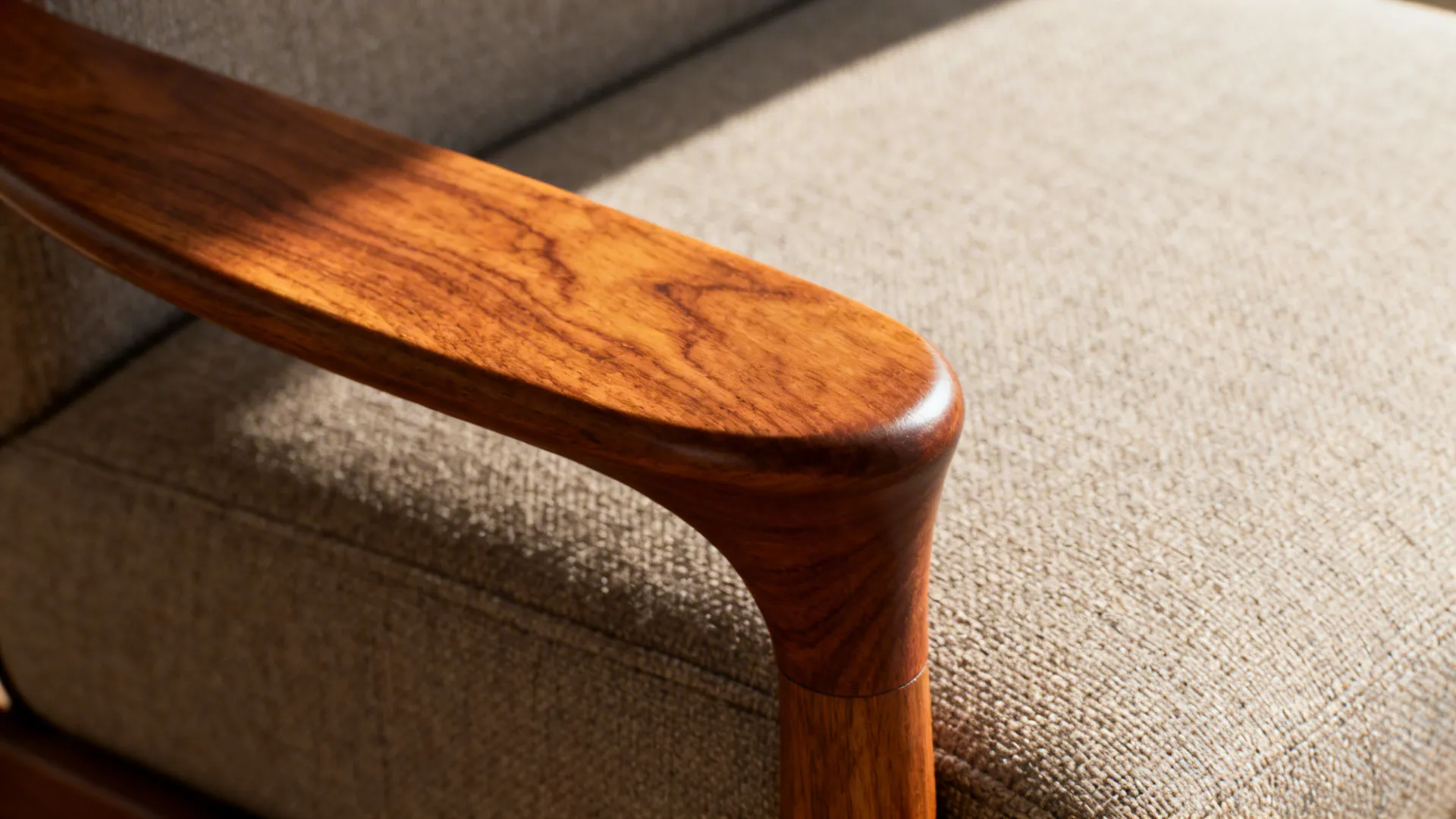 Close-up of a sculpted walnut armrest and textured upholstery on a mid-century sofa.