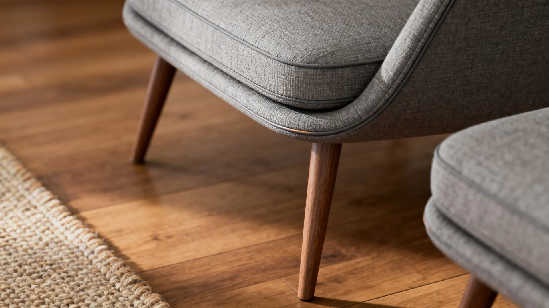Close-up of a slim midcentury gray chair and ottoman showing tapered legs and textured fabric.