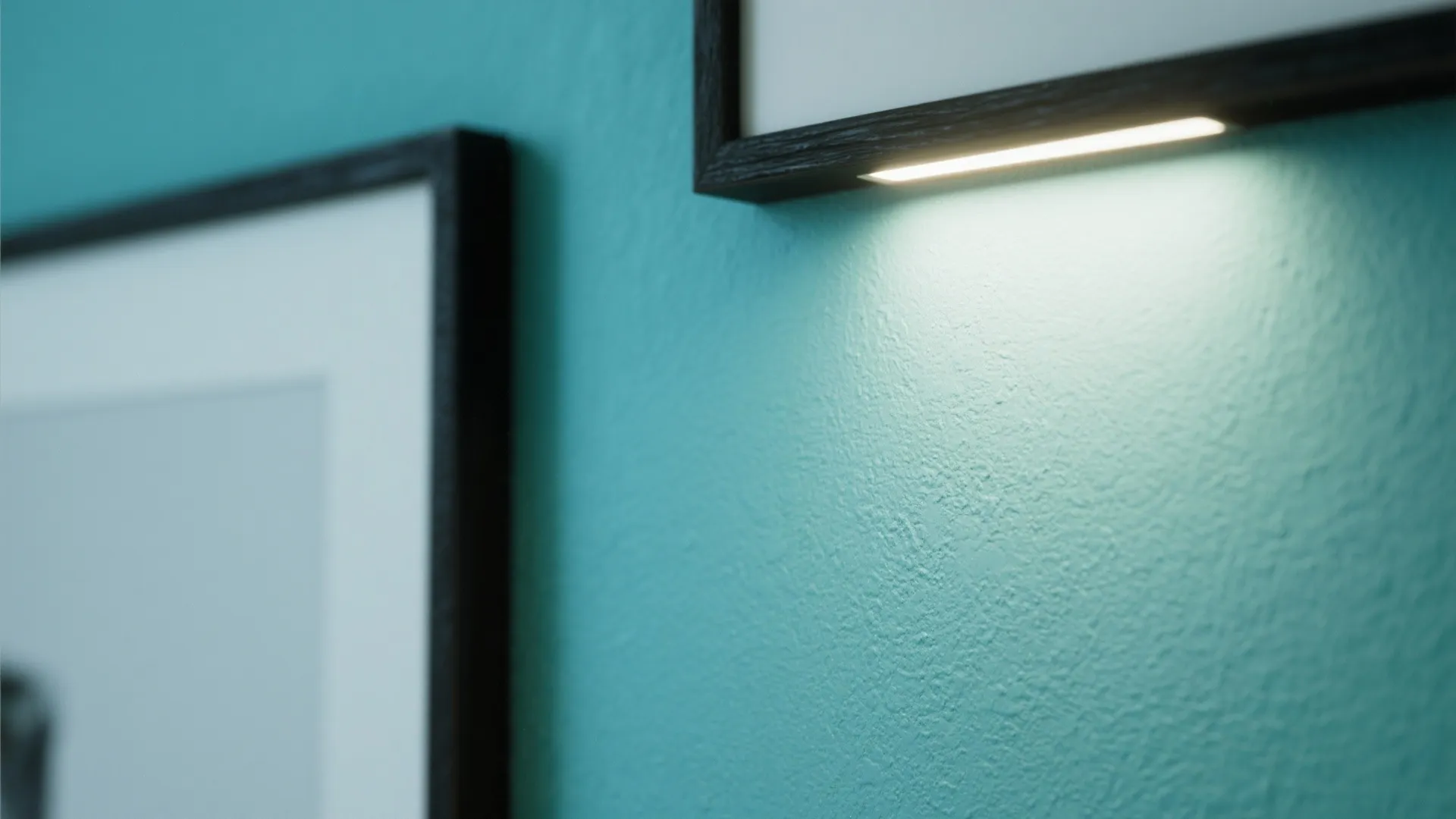 Close-up of matte blue-green wall beside a black frame under soft sconce lighting.