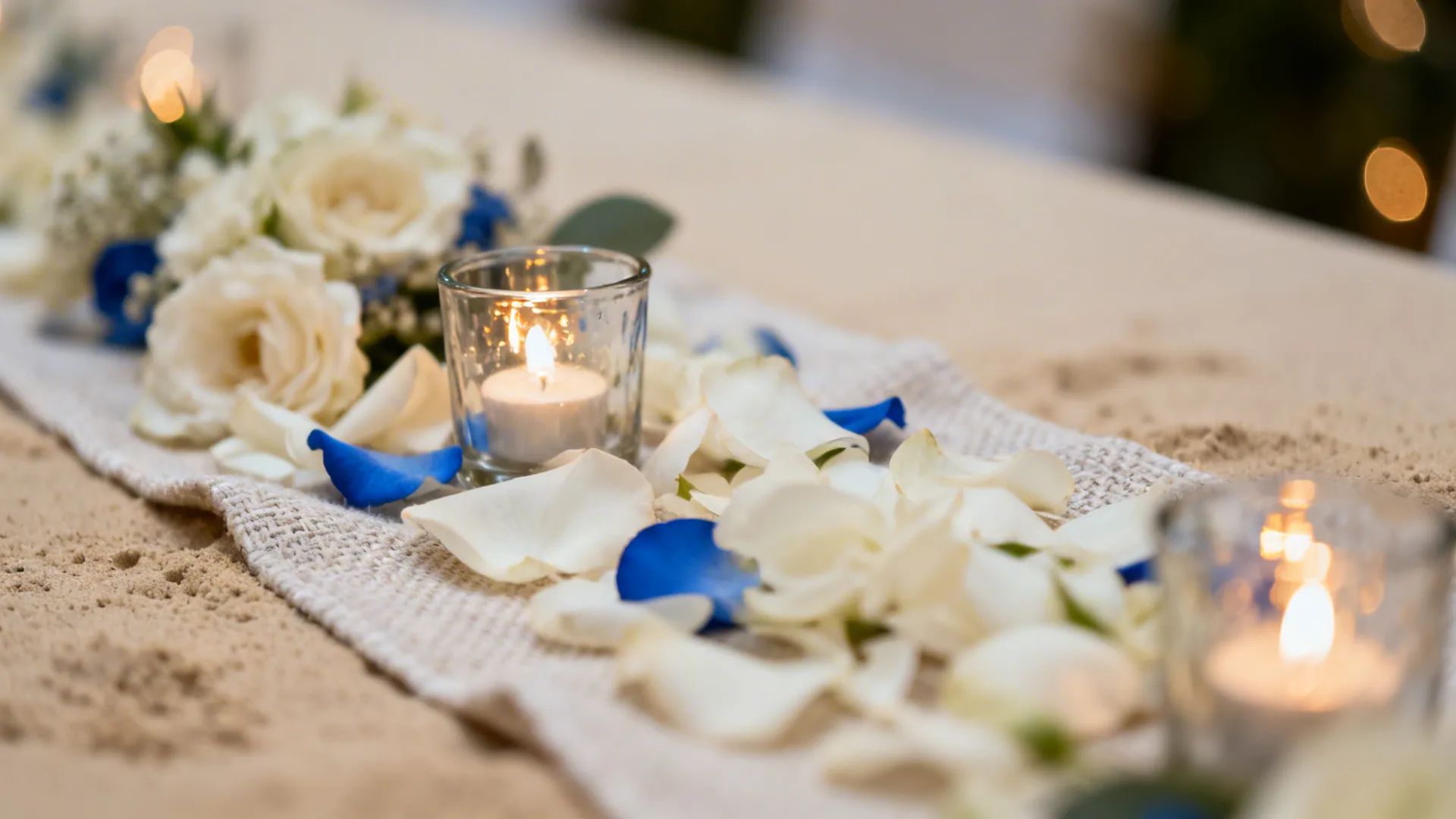 Macro close-up of a low floral centerpiece with glass votives on a cloth runner.