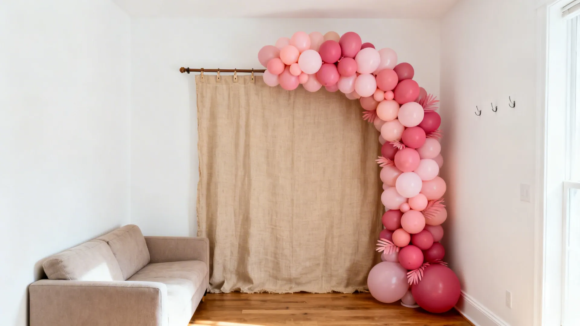 Half-arch balloon garland and a linen backdrop create a tidy birthday photo zone in a small room.