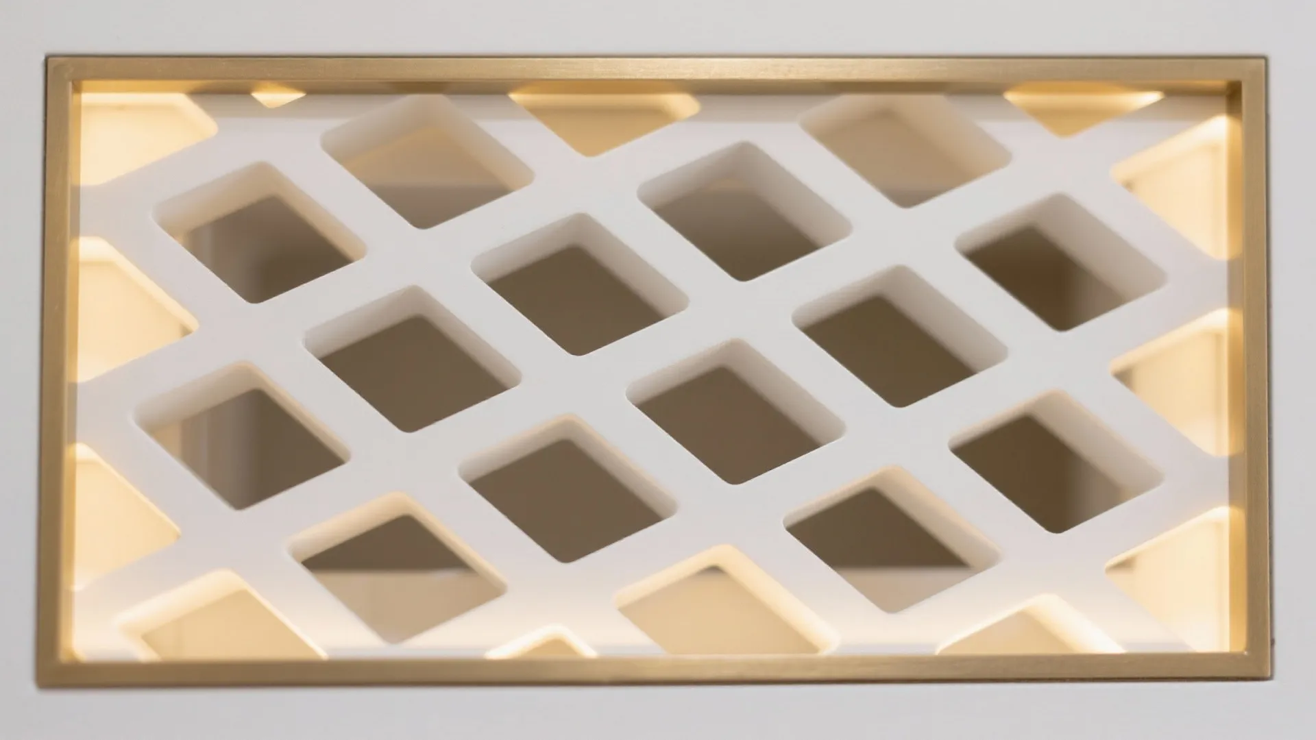 Macro detail of matte white geometric MDF jali with slim brass trim and soft backlighting.