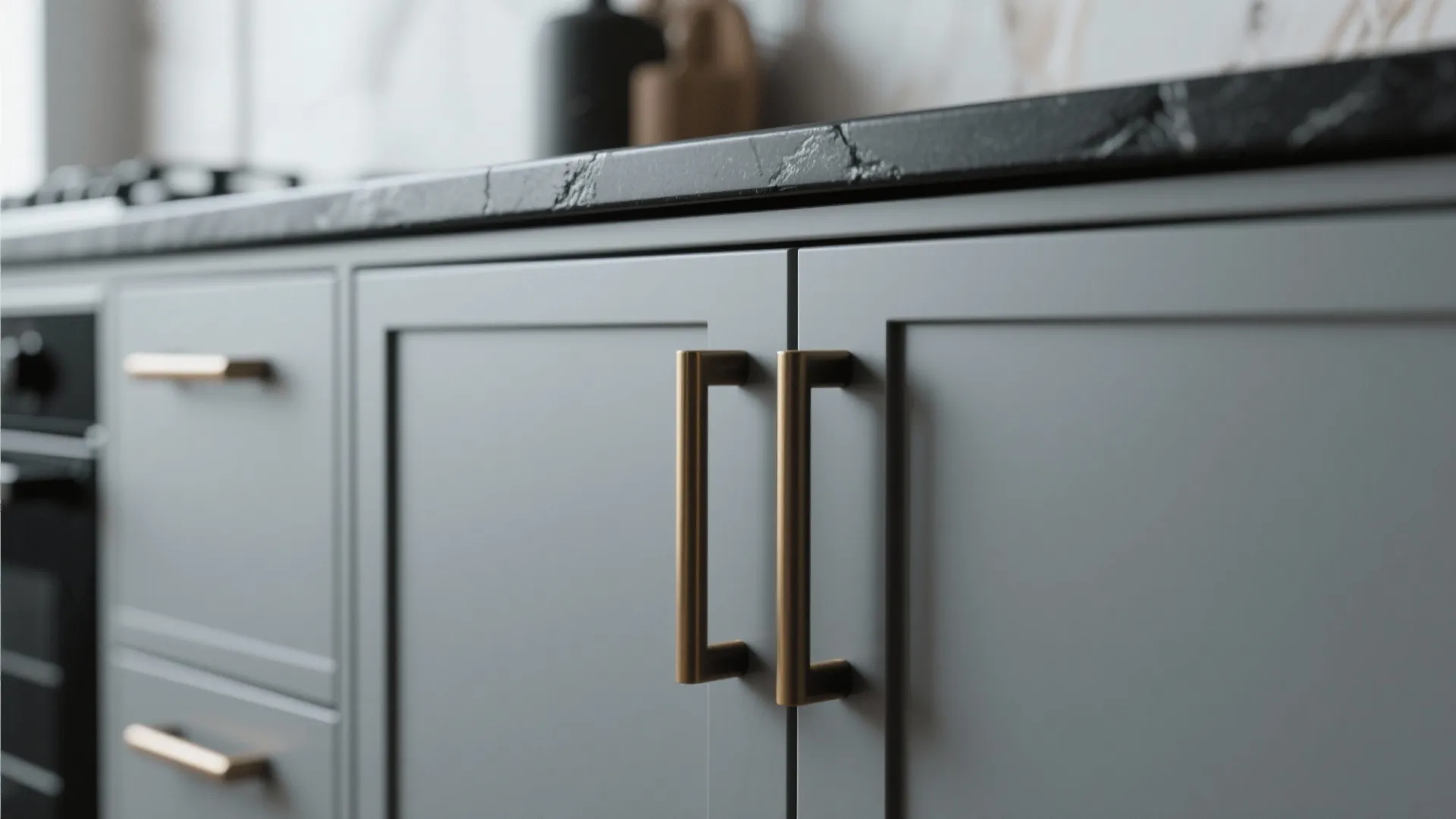 Minimal black and brushed brass hardware on gray cabinets above a black countertop.