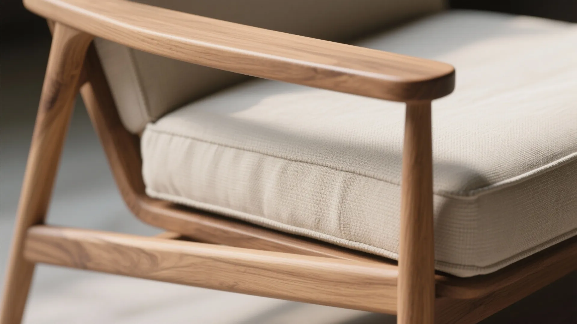 Close-up of oak arm and linen cushion on a minimalist lounge chair, showing fine grain and stitching.