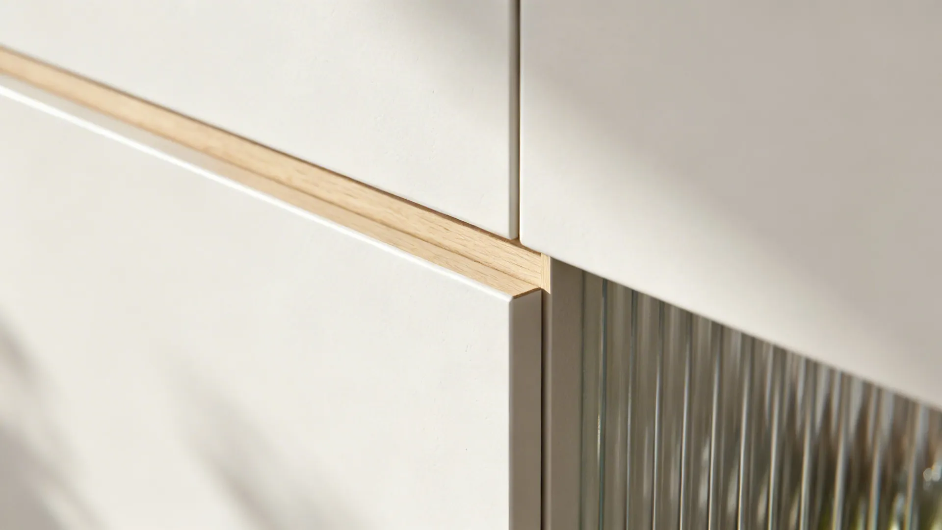 Macro of matte white cabinet with thin light-oak edge and ribbed glass in soft light.