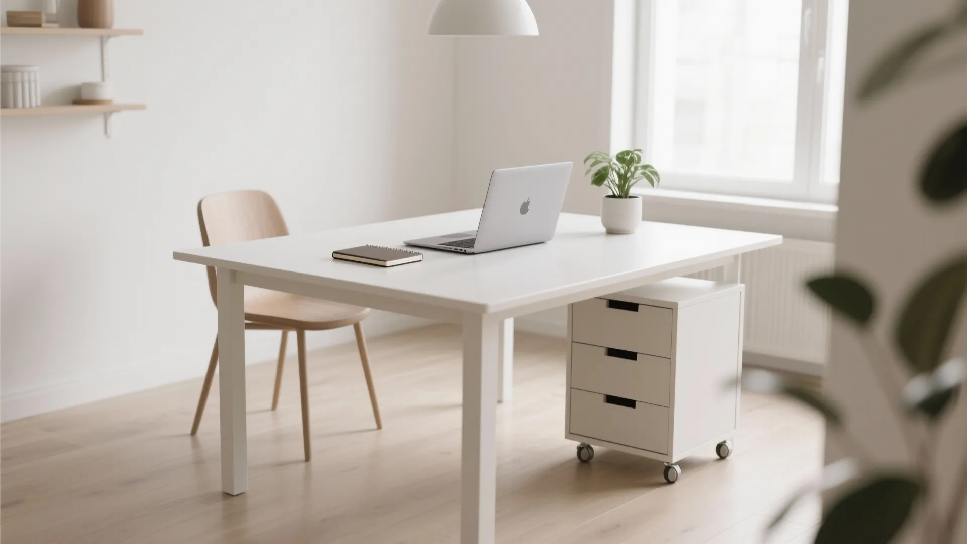 Minimalist white home office desk with laptop small plant wooden chair and white storage cabinet