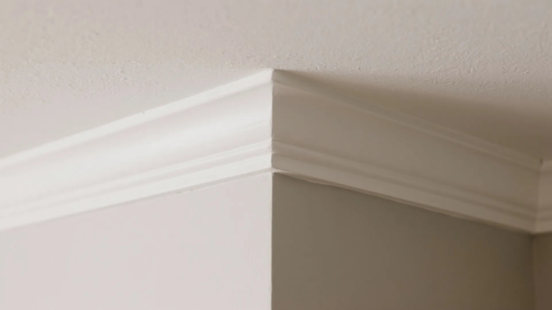Close up view of white decorative ceiling trim meeting a corner of neutral colored walls