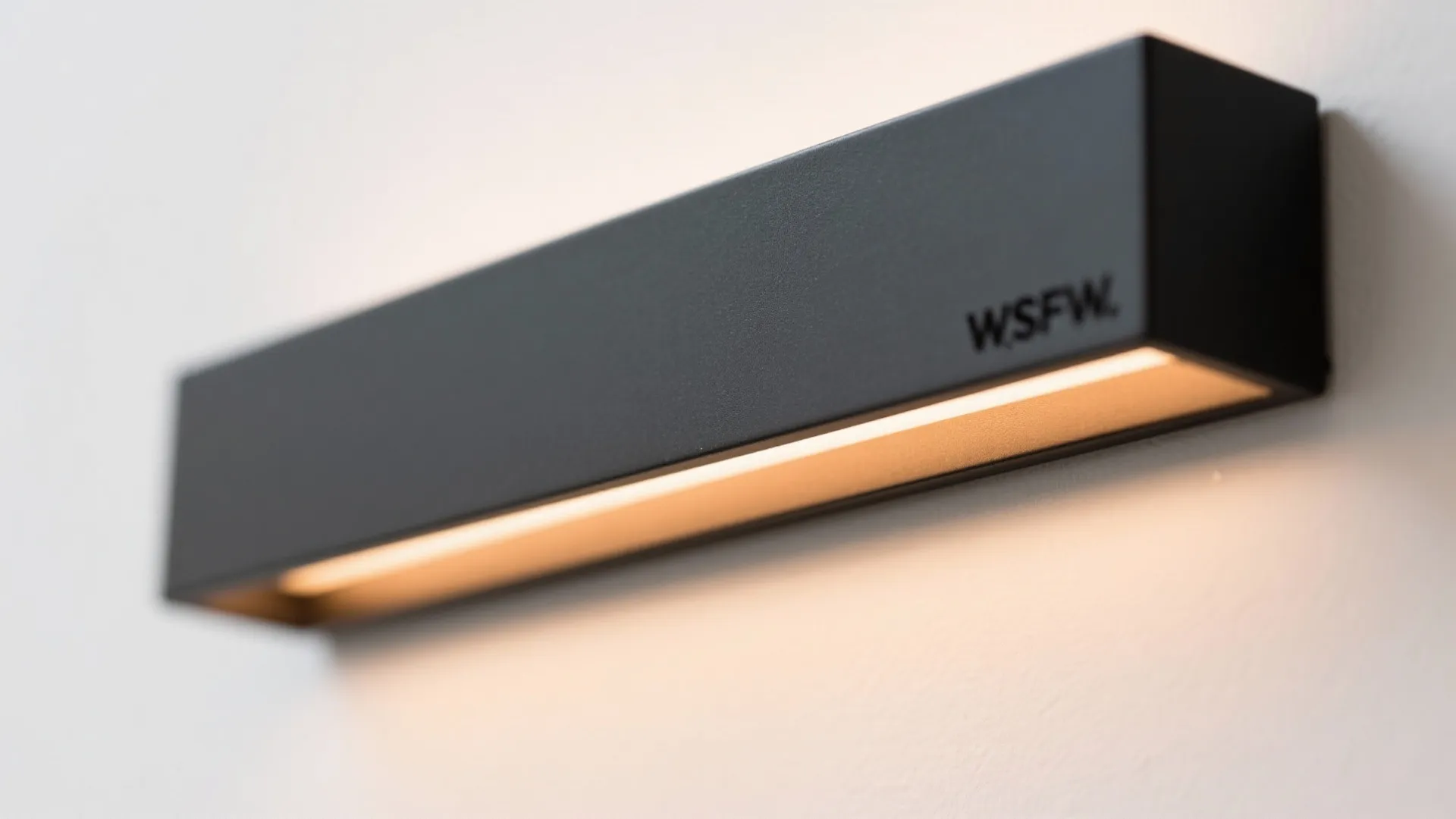 Modern black rectangle wall light with warm glow shining downwards on a plain white wall