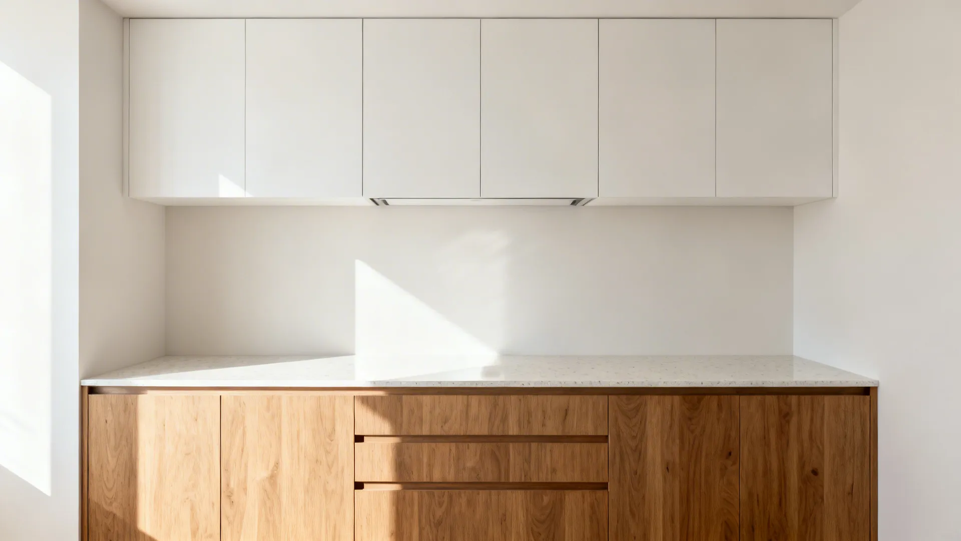 Minimalist kitchen design featuring white upper cabinets wood lower drawers and a clean white countertop