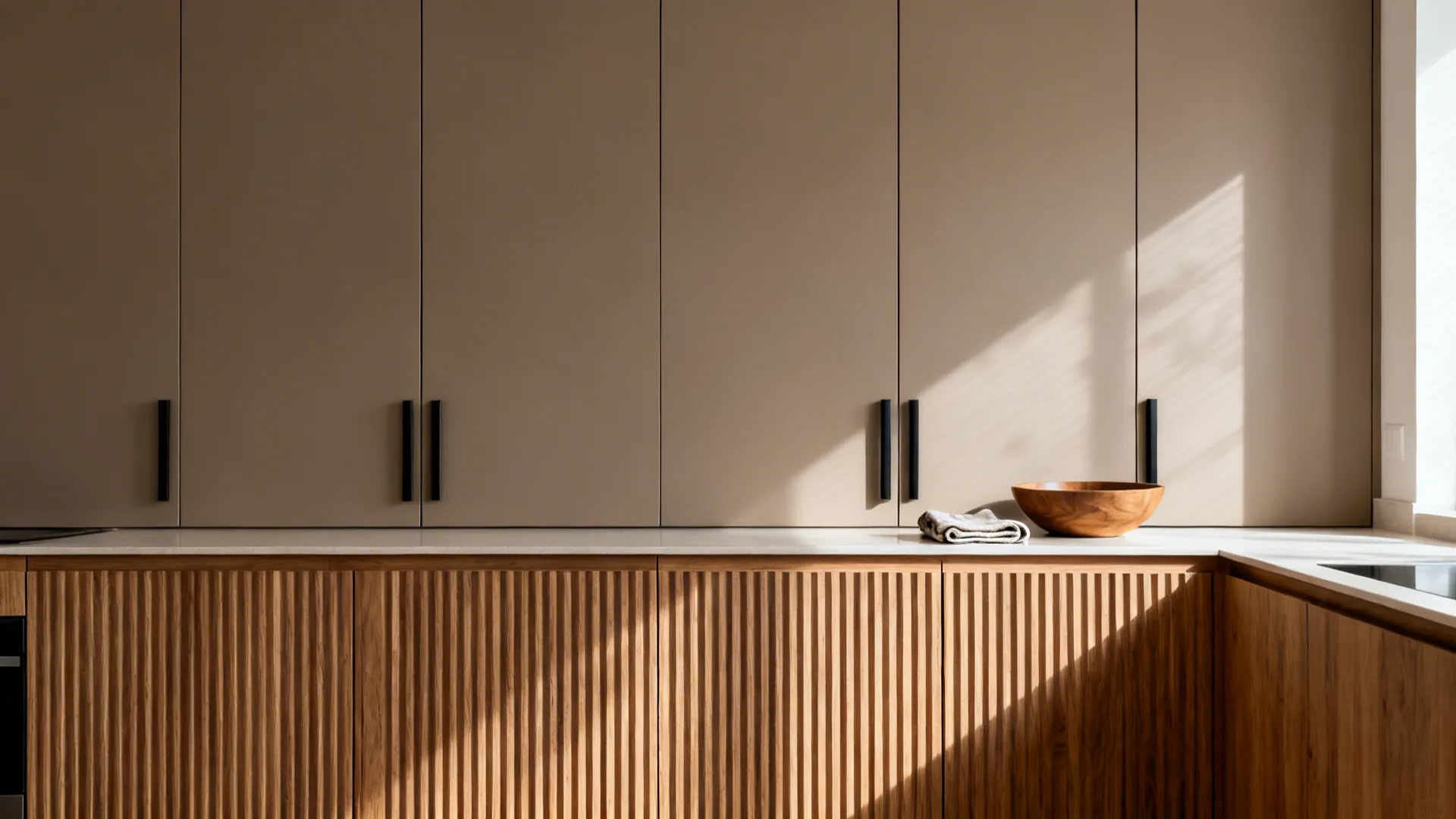 Matte taupe flat-panel cabinets with ribbed oak accents and slim black pulls in a small kitchen.