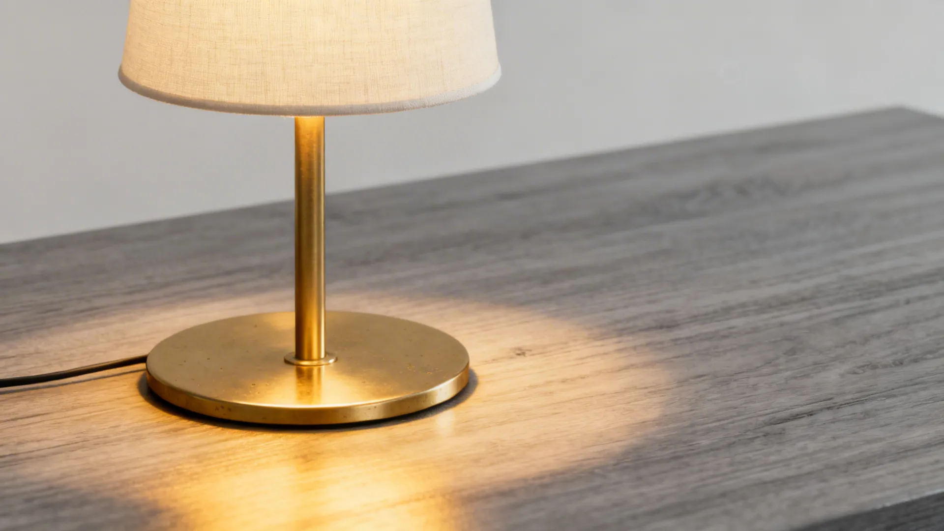 Close-up of a slim minimalist brass lamp with warm LED glow on a neutral side table.