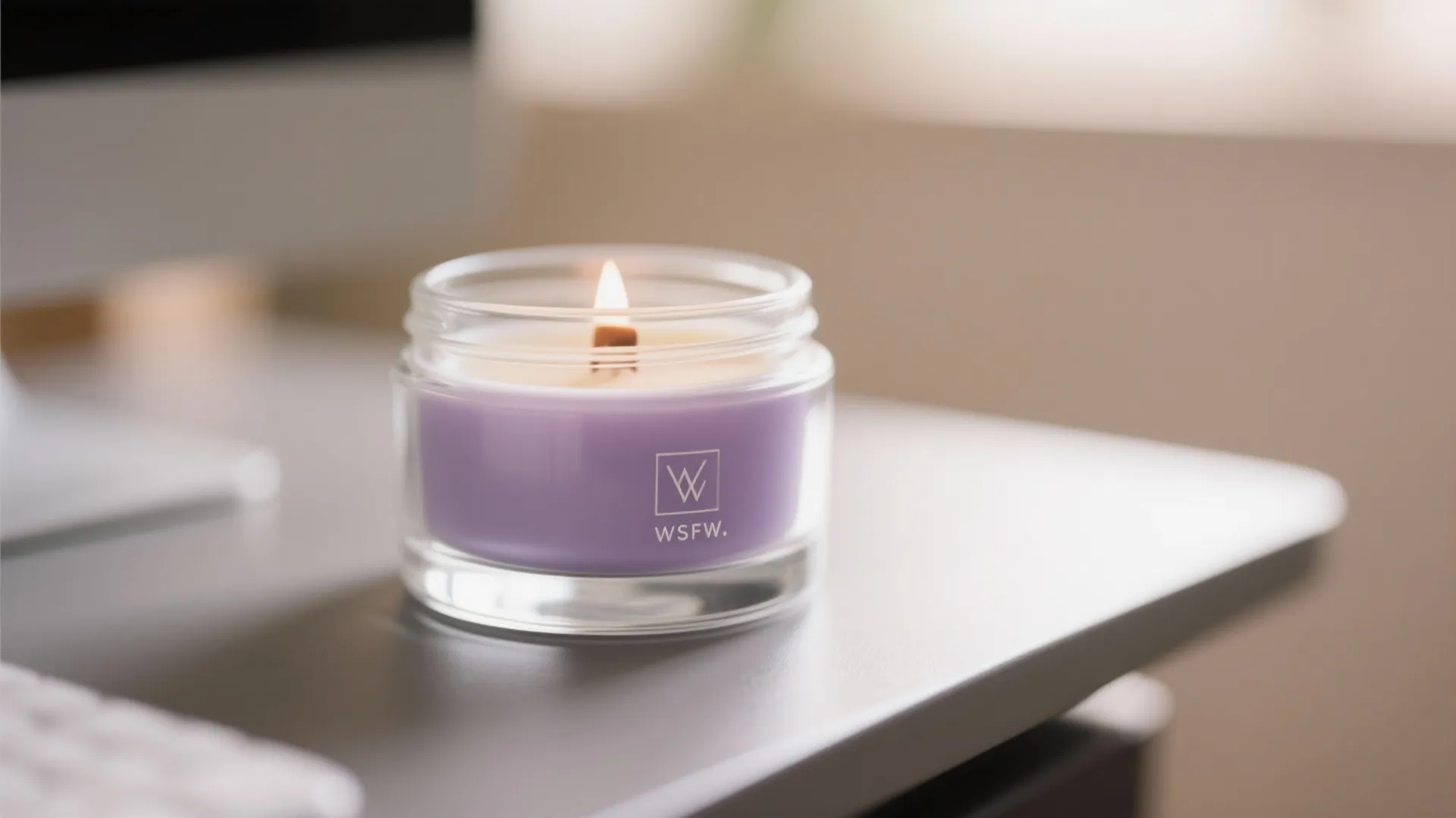 Lit purple scented candle in a glass jar sitting on a modern office desk setup