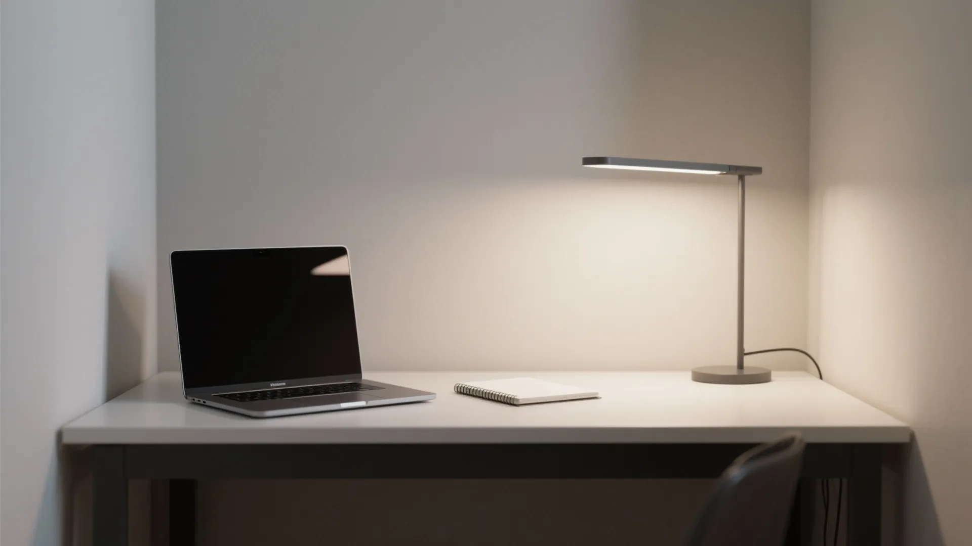 Minimalist white desk featuring a laptop computer and small notebook under a modern desk light