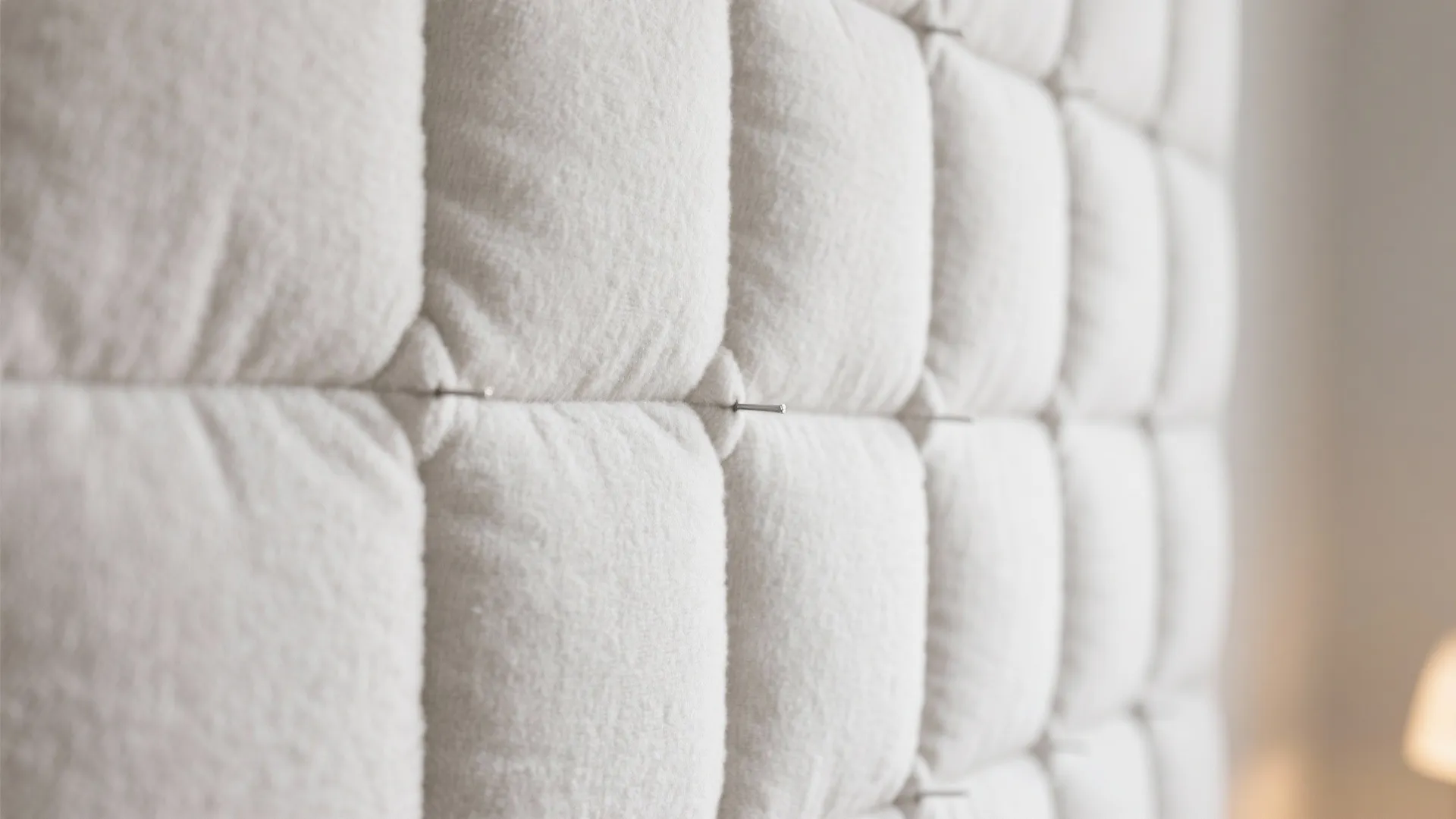 White soft wall panel with padded square sections and small metal pins in a room