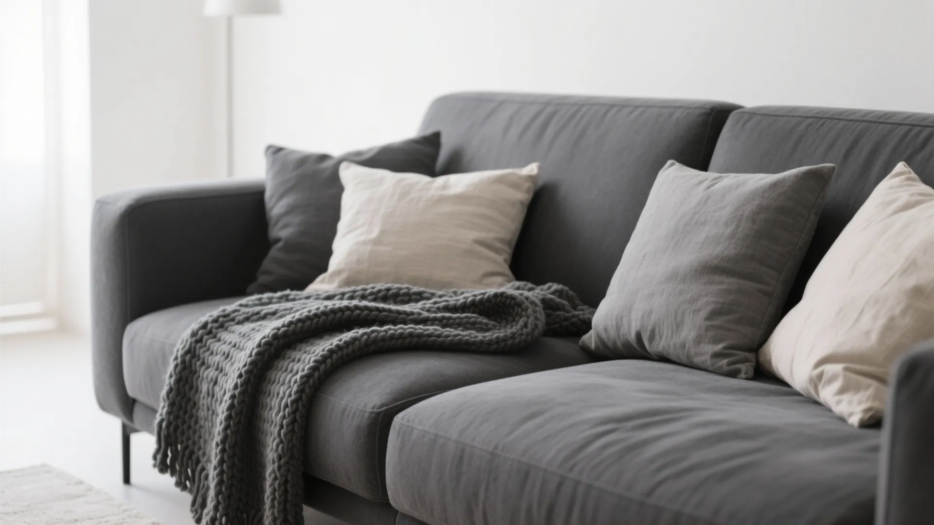 Close up of a dark grey sofa with light pillows and a knitted wool blanket throw