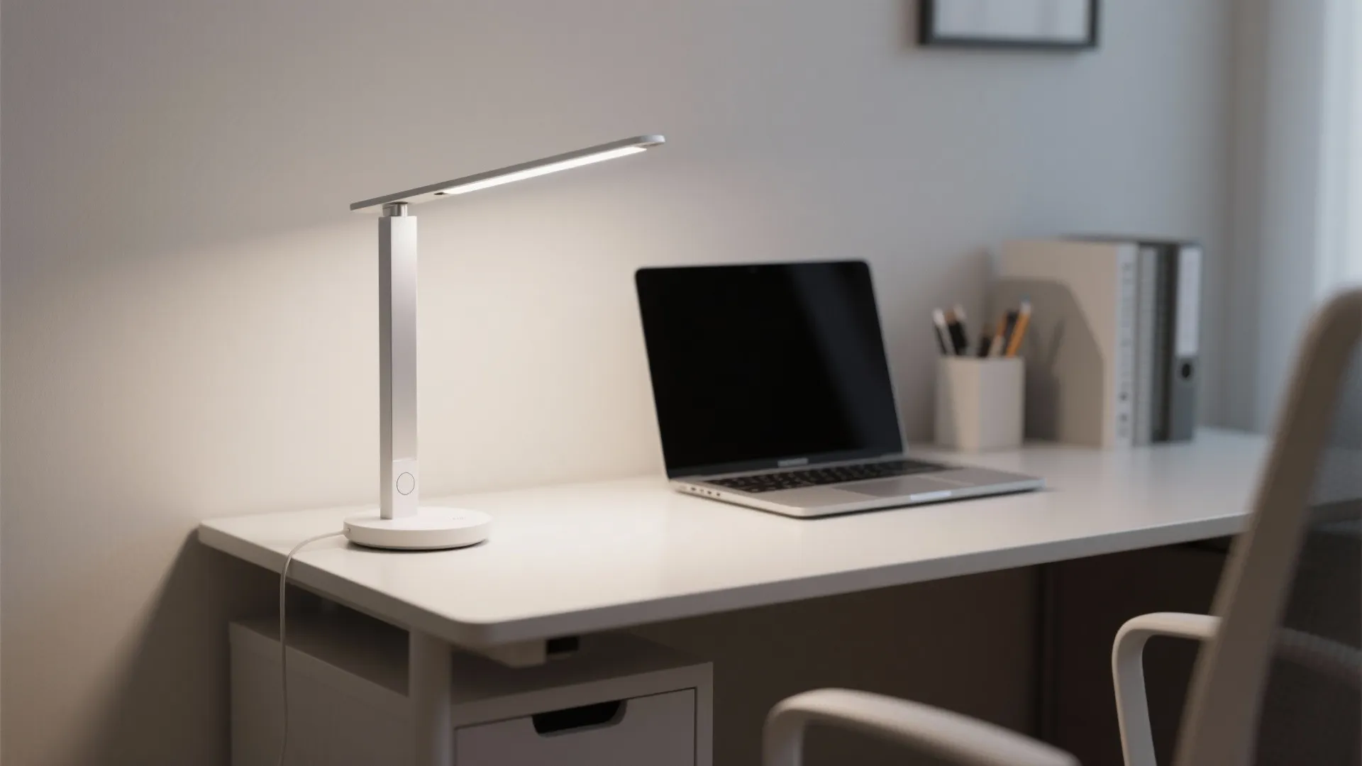 Modern white desk with a silver LED lamp a laptop and a white chair nearby