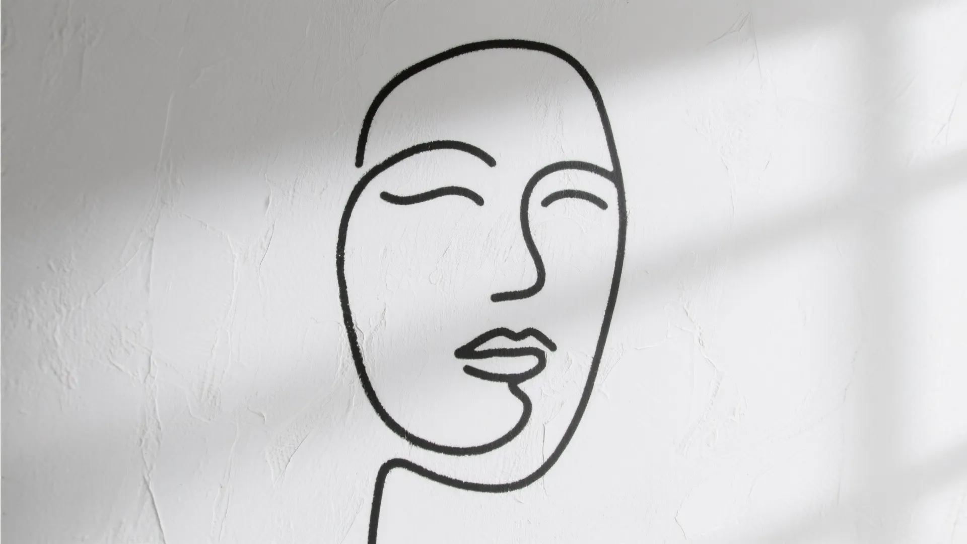 Simple black line art of a human face on a white textured wall with natural shadows