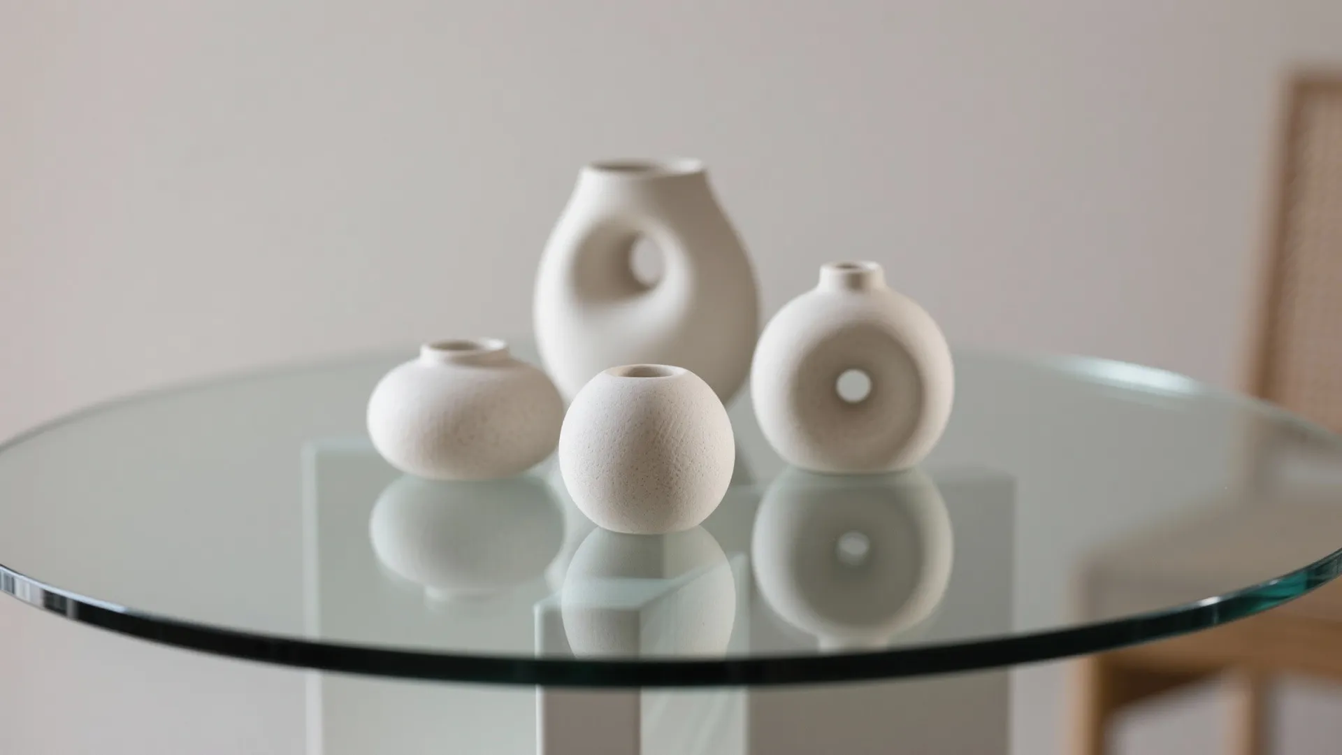 Four white ceramic vases in different shapes placed on a glass table in bright room