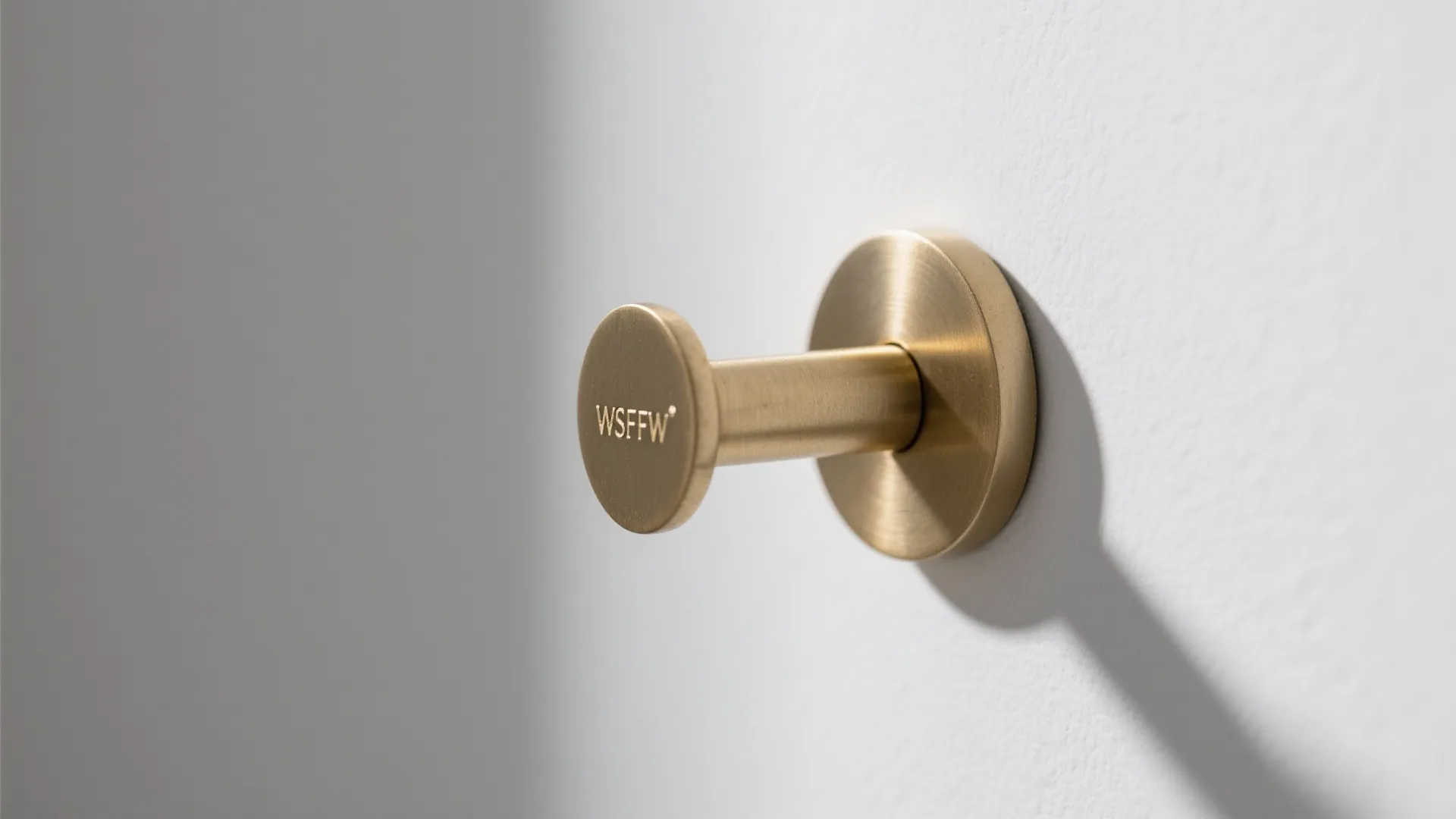 Modern gold wall hook mounted on a white wall with soft light and shadows cast
