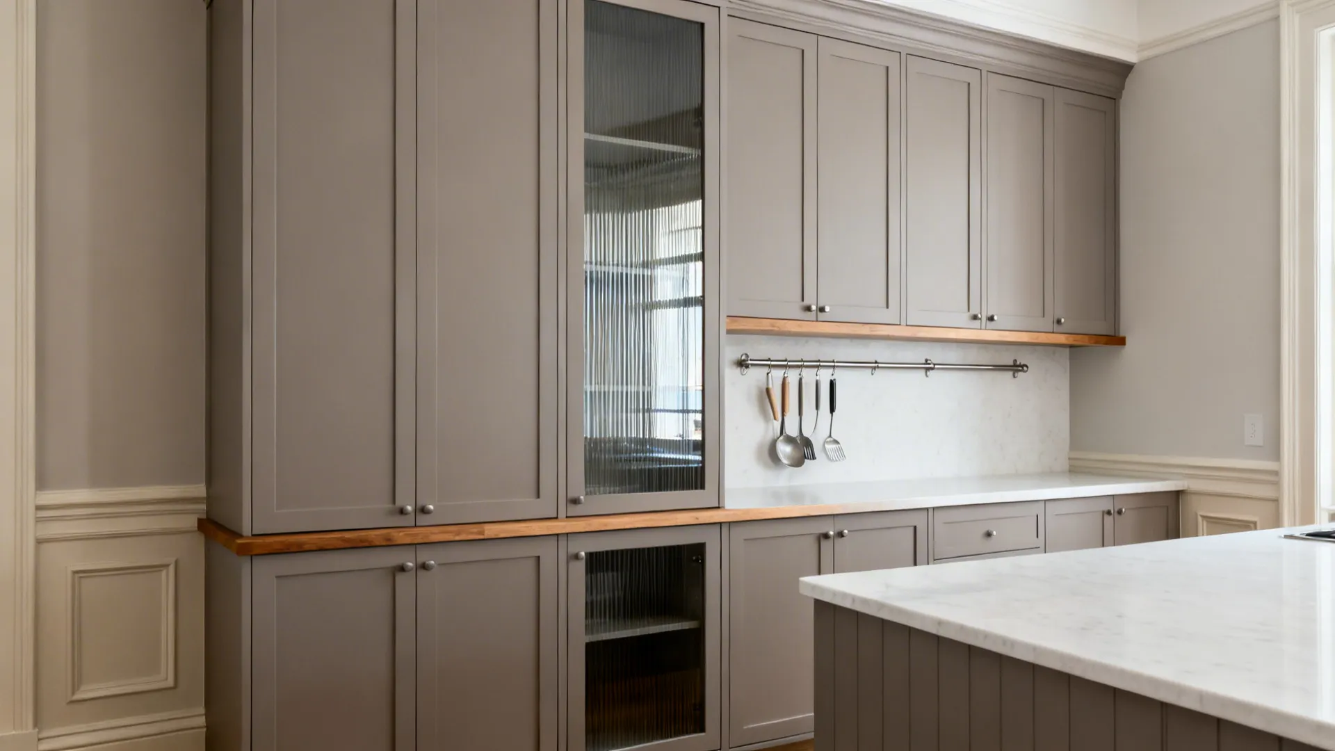 Full-height pantry cabinets with ribbed-glass doors and a neat rail keep a small kitchen serene.
