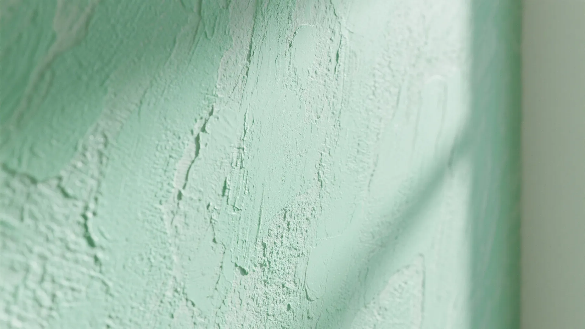 Close-up of a mint-green textured wall finish showing lime-wash or micro-sponge texture and tonal variation.