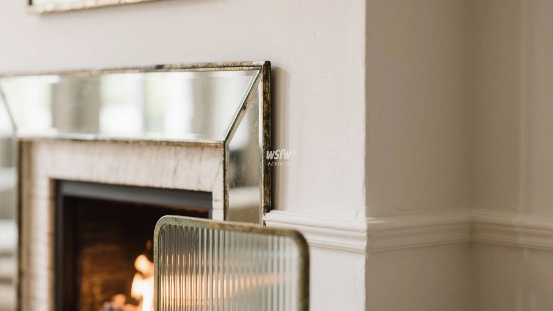 Close up of a wall mirror with a gold frame above a fireplace with burning wood