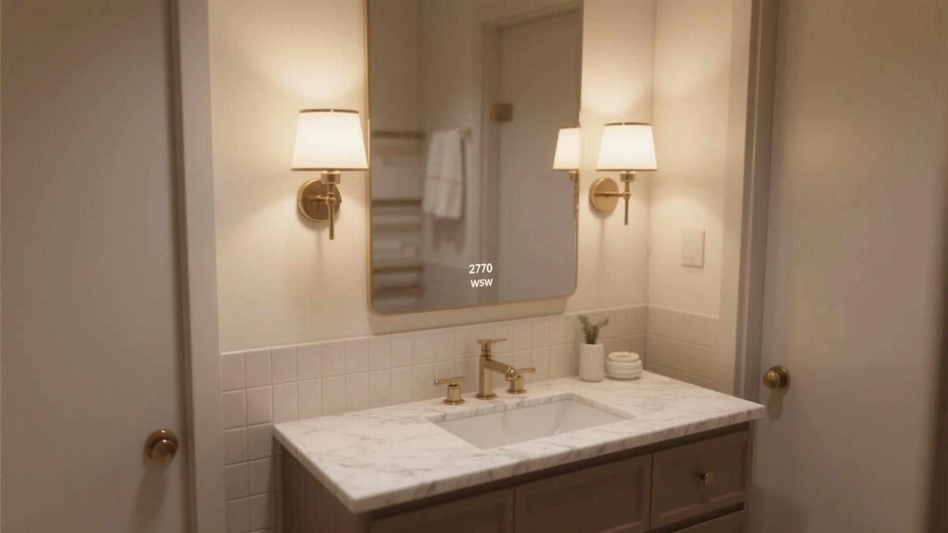 Bathroom vanity with marble top white sink and two gold wall lights beside the mirror