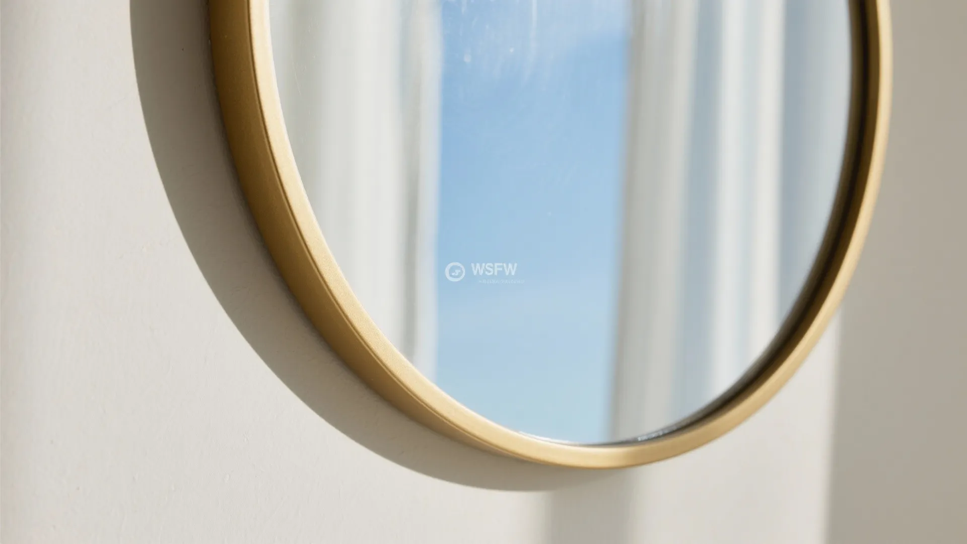 Close up view of a round wall mirror with a gold frame reflecting bright blue sky