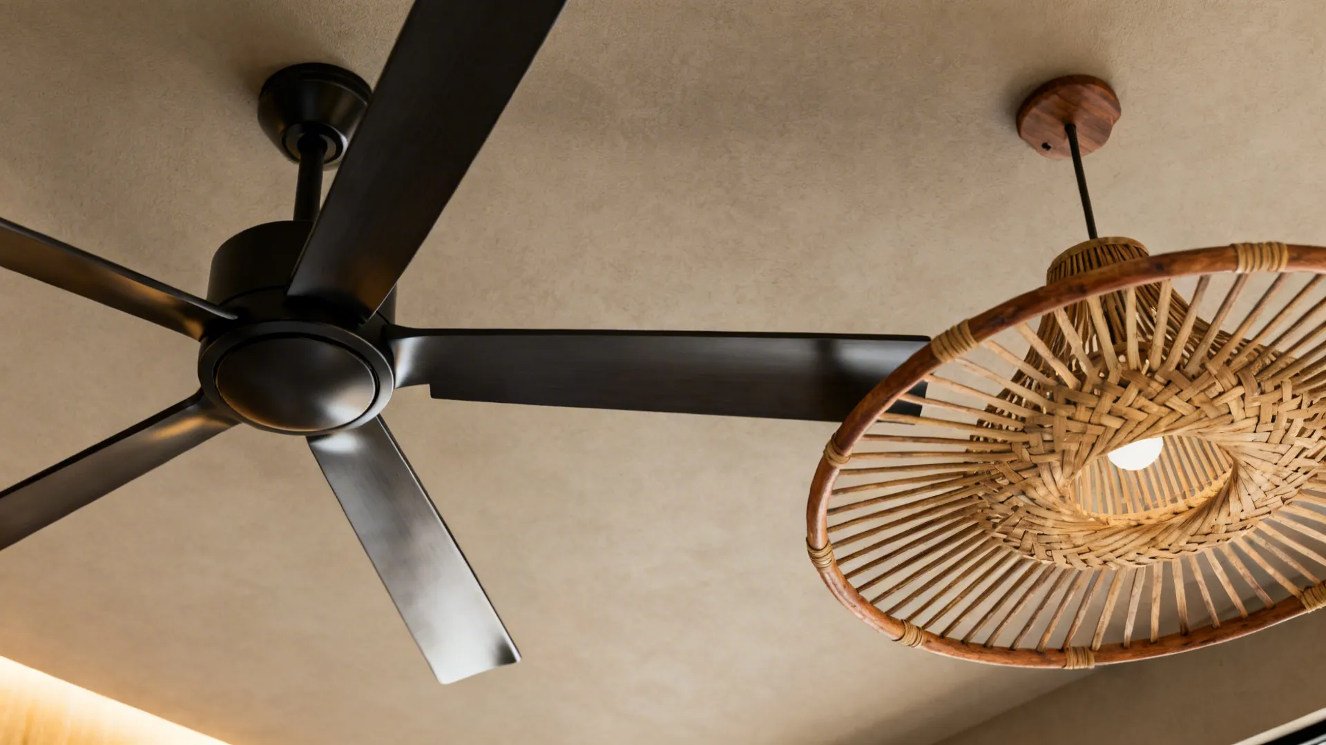 Close-up of two ceiling fans with contrasting finishes: matte black and natural wood rattan.