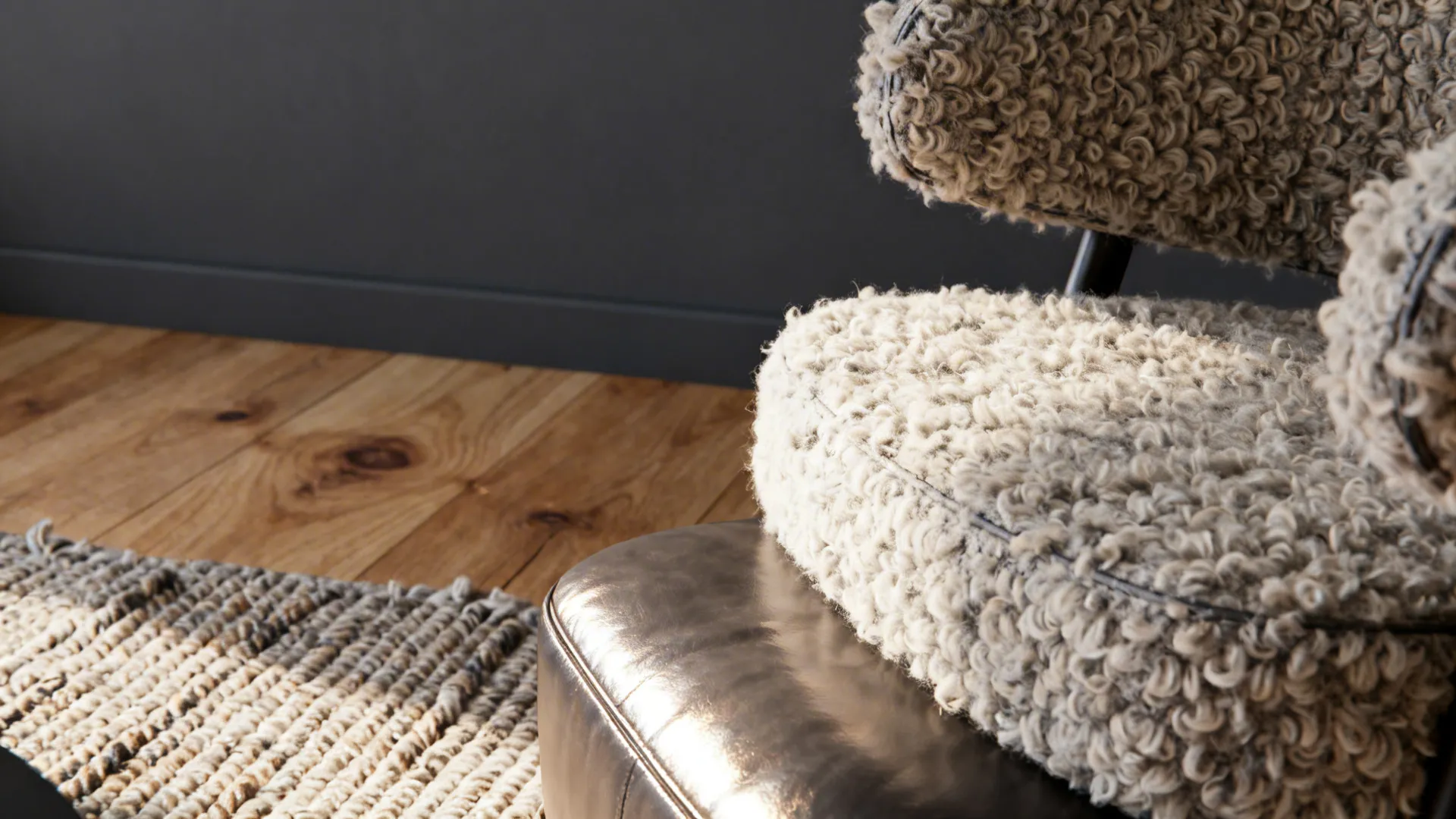 Close-up of boucle chair, leather ottoman, and textured rug against dark gray walls.