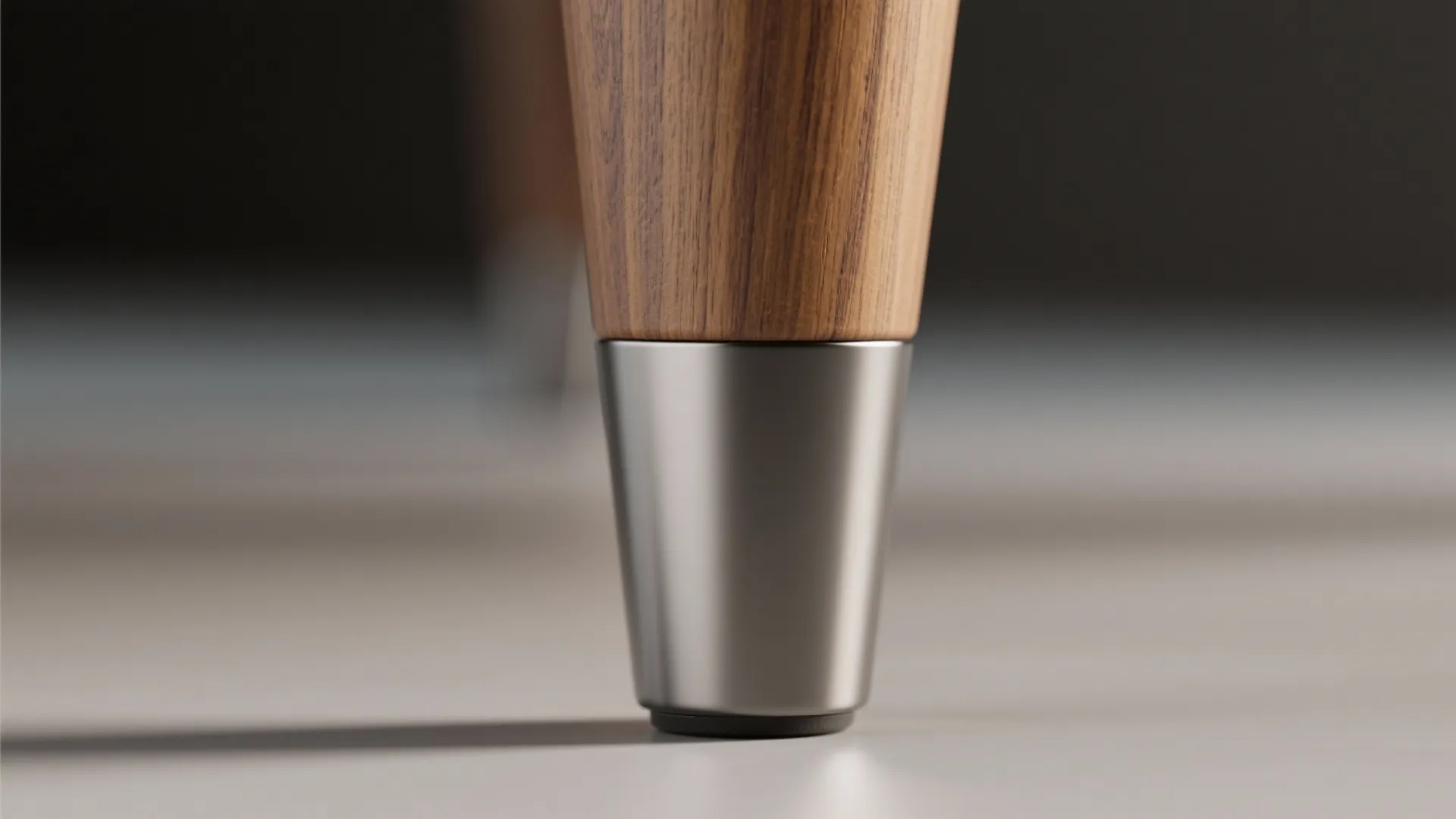 Close up of a wooden furniture leg with a tapered silver metal cap on the floor