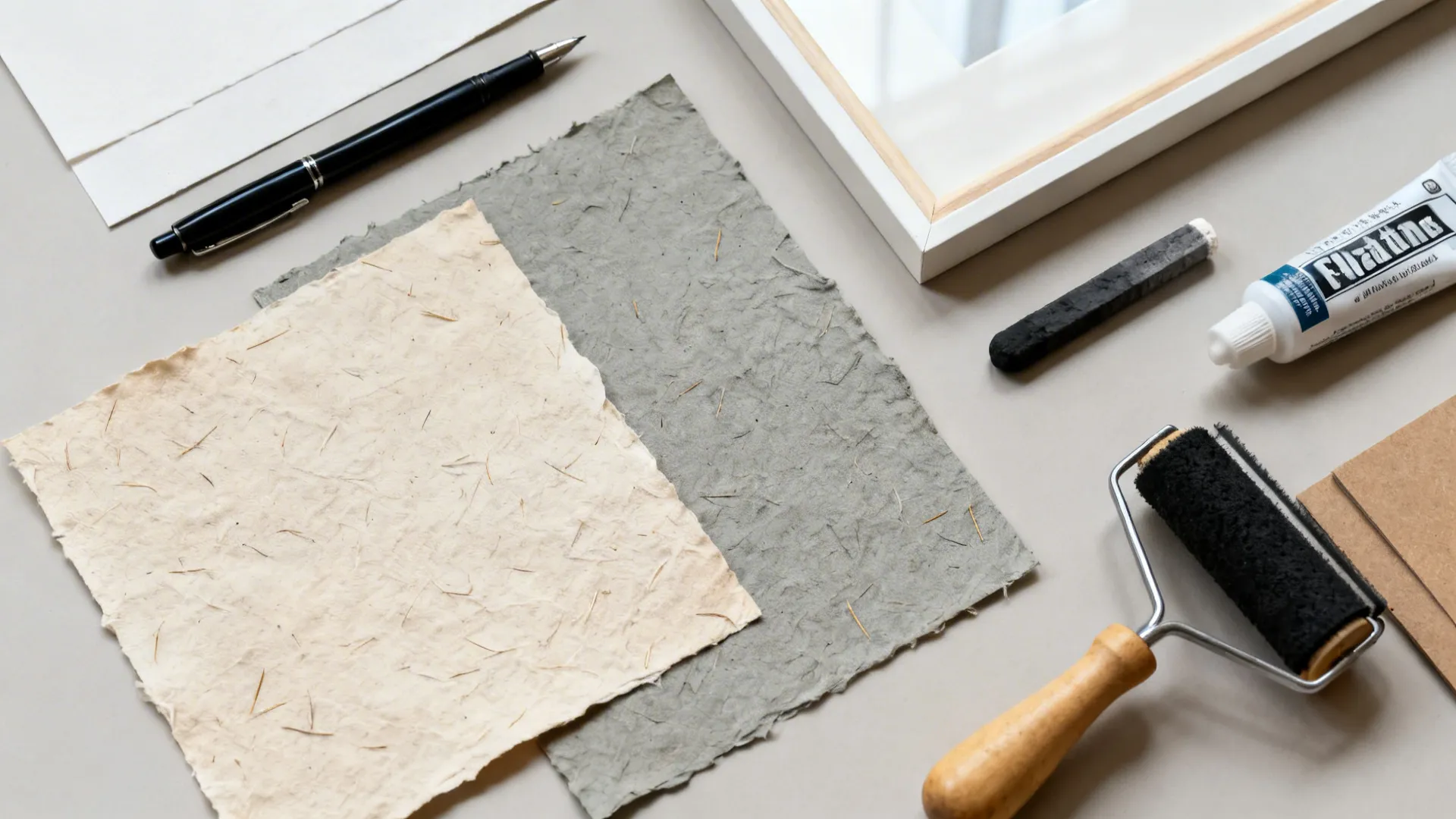 Top-down layout of handmade papers, ink, glue, brayer, and floating frame.
