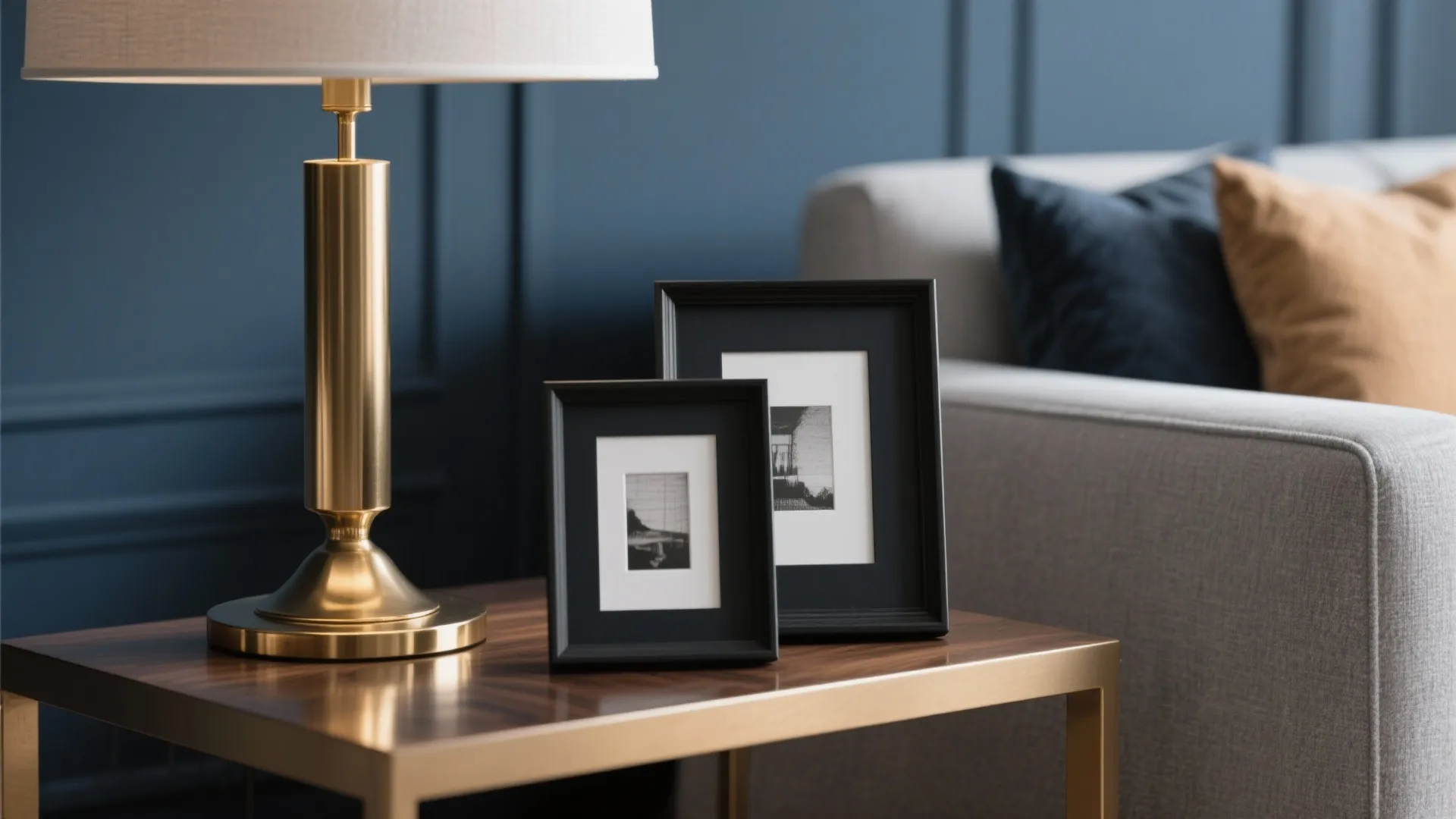 Gold table lamp and two black picture frames on a wooden side table near gray sofa