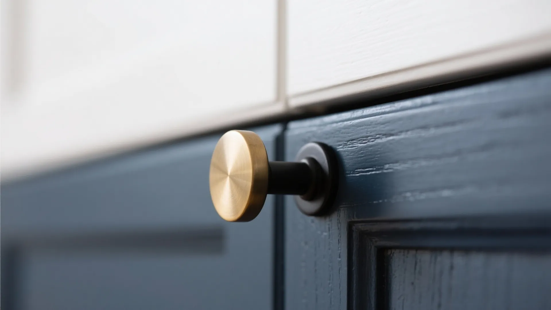 Gold round knob on dark blue kitchen cabinet door below white upper wooden wall panel