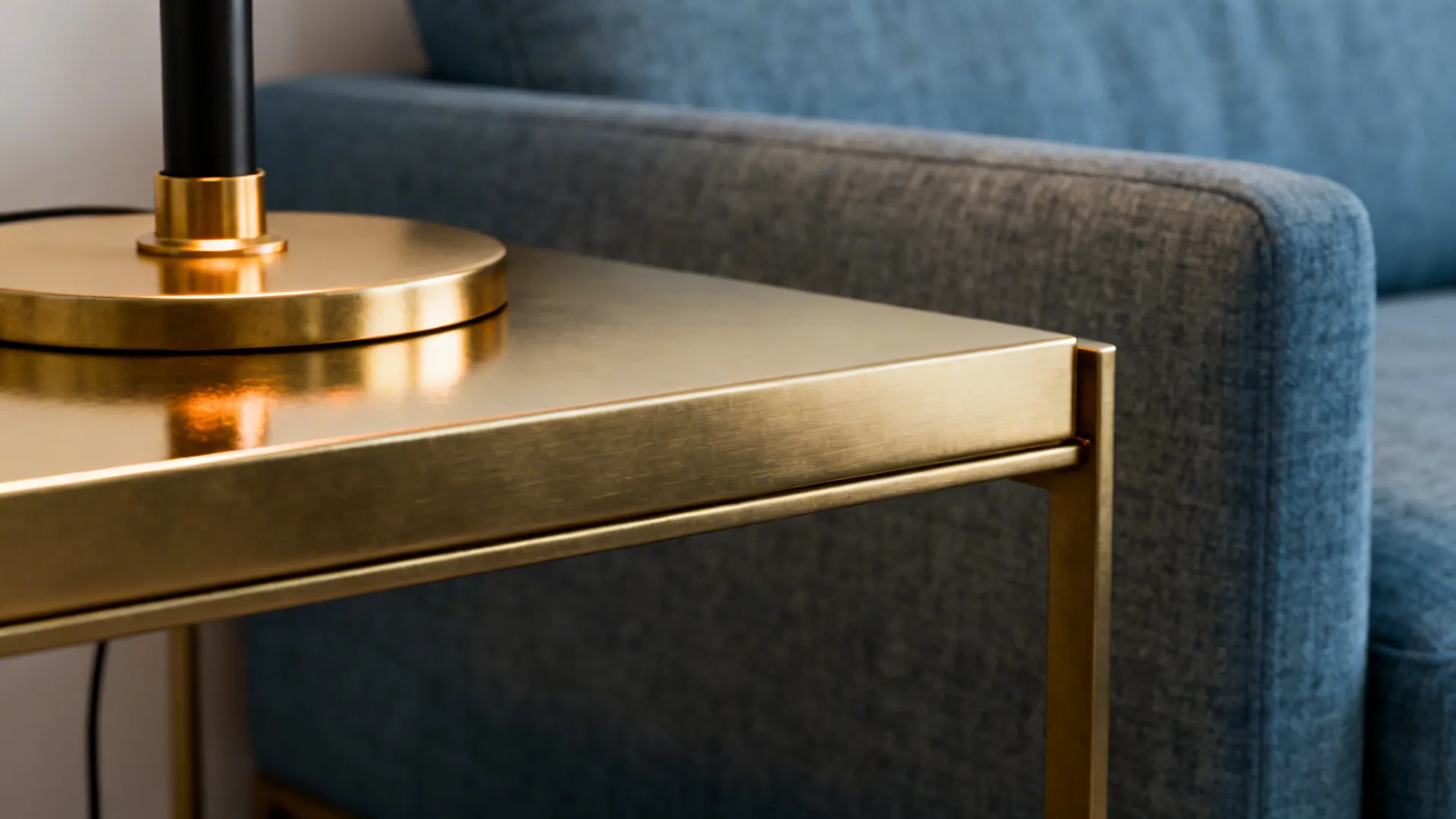 Close-up of brushed brass side table and matte black lamp near a blue-grey sofa
