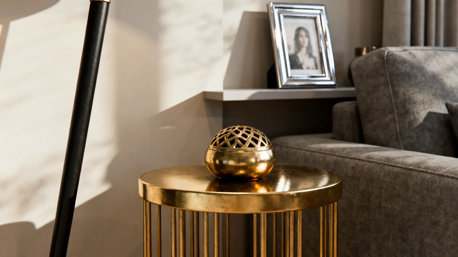 Brass side table, matte-black lamp leg and chrome frame near a grey sofa