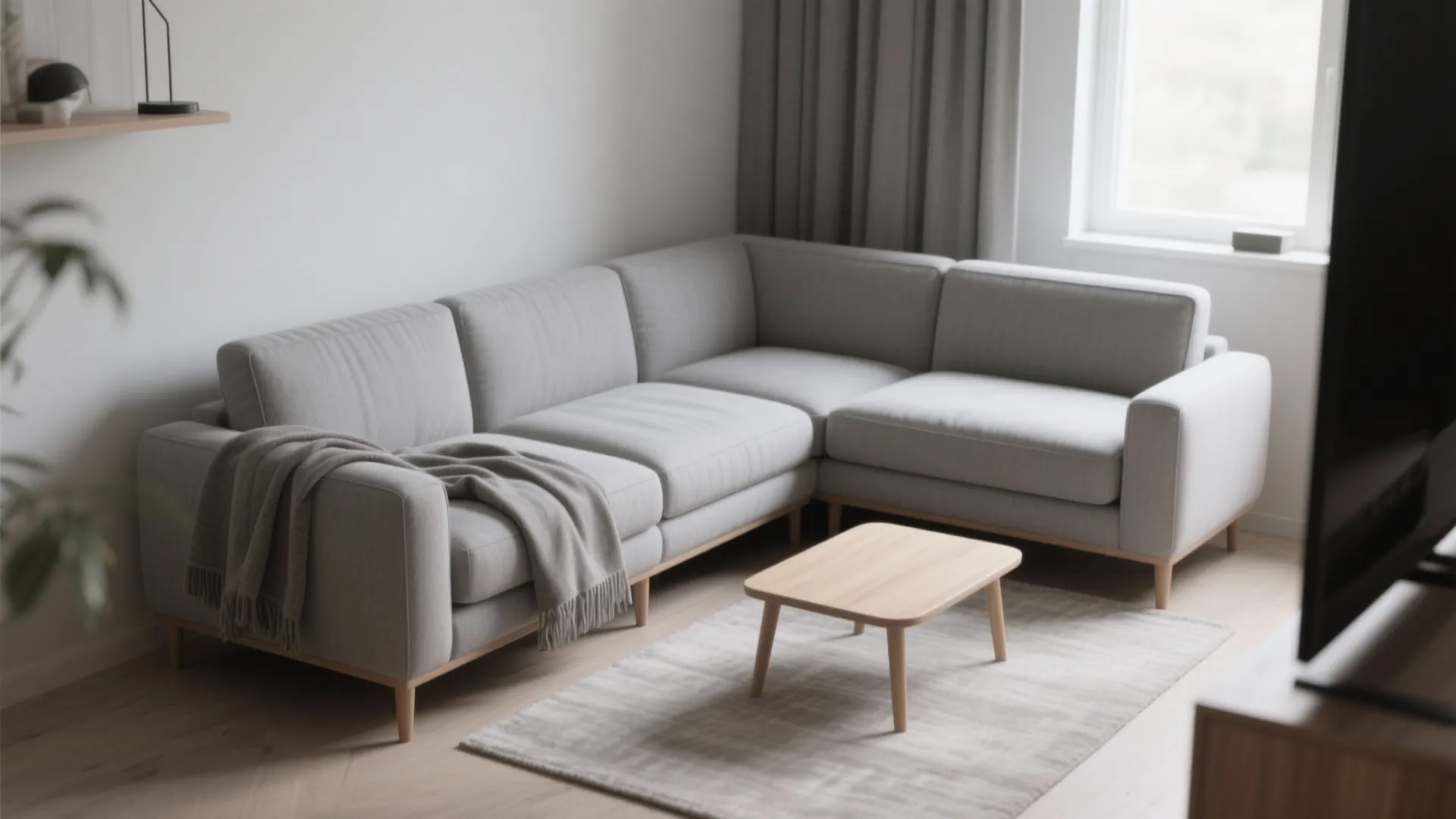 Grey corner sofa with grey blanket next to small wooden coffee table on light rug