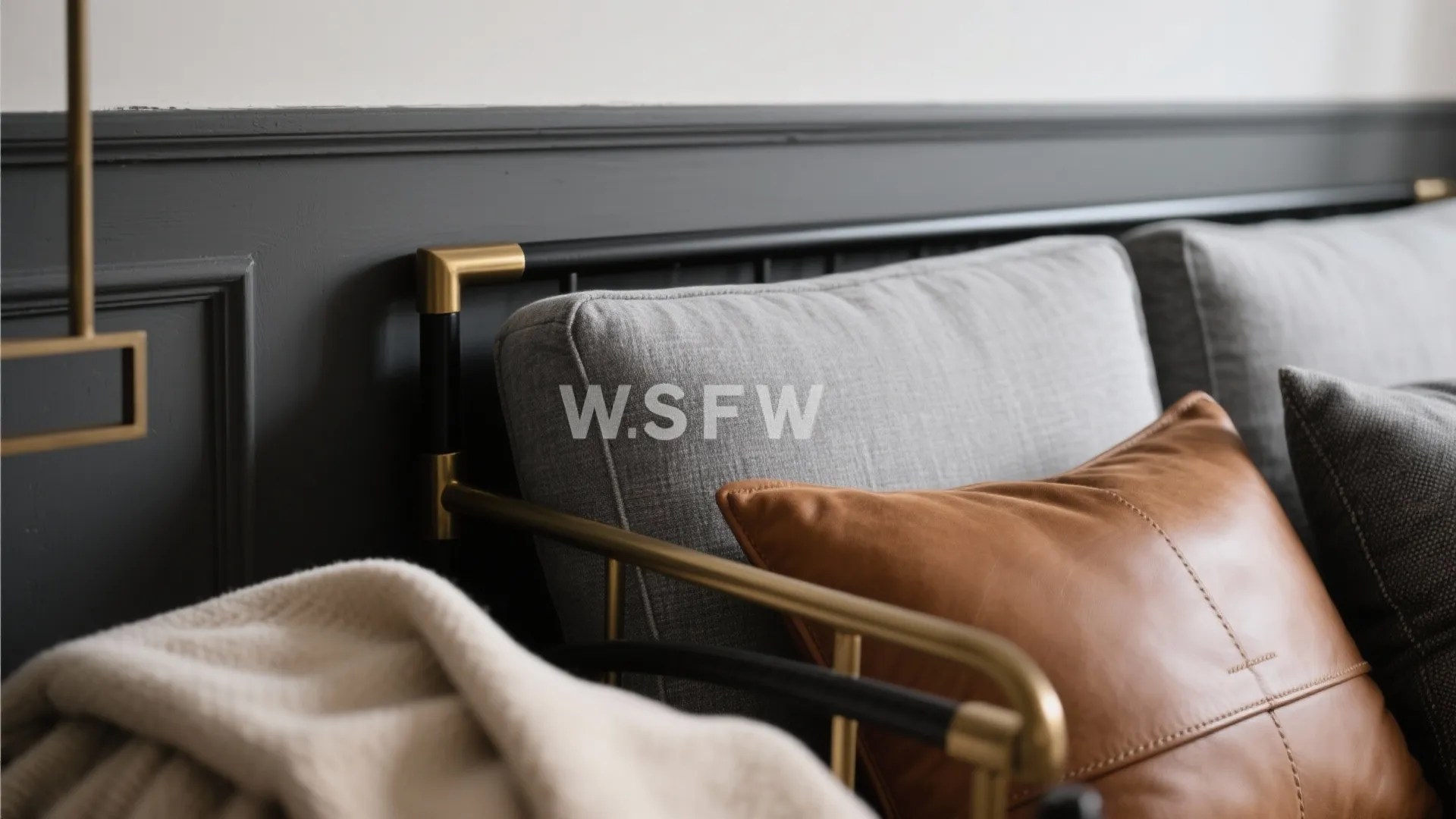 Close up of a grey sofa with brown leather pillow and a dark wall panel