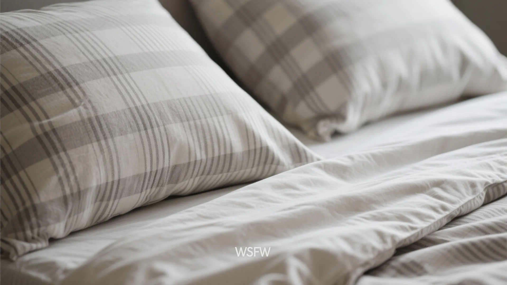 Close-up of two grey and white plaid pillows on a soft white bed with duvet