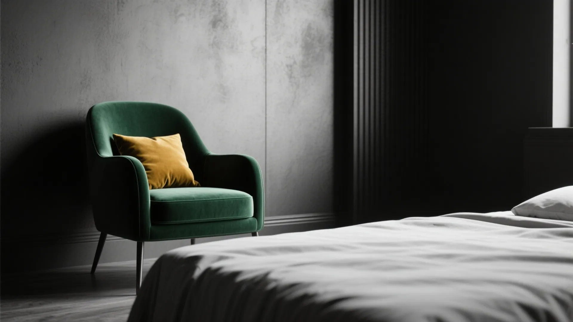 Green velvet chair with yellow pillow in a dark bedroom with grey wall and bed