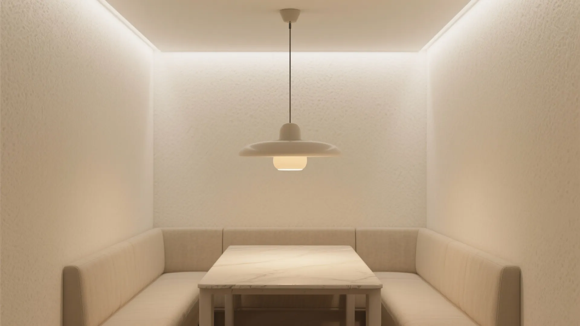 Minimalist dining nook with cream bench seating marble table and a single white ceiling light