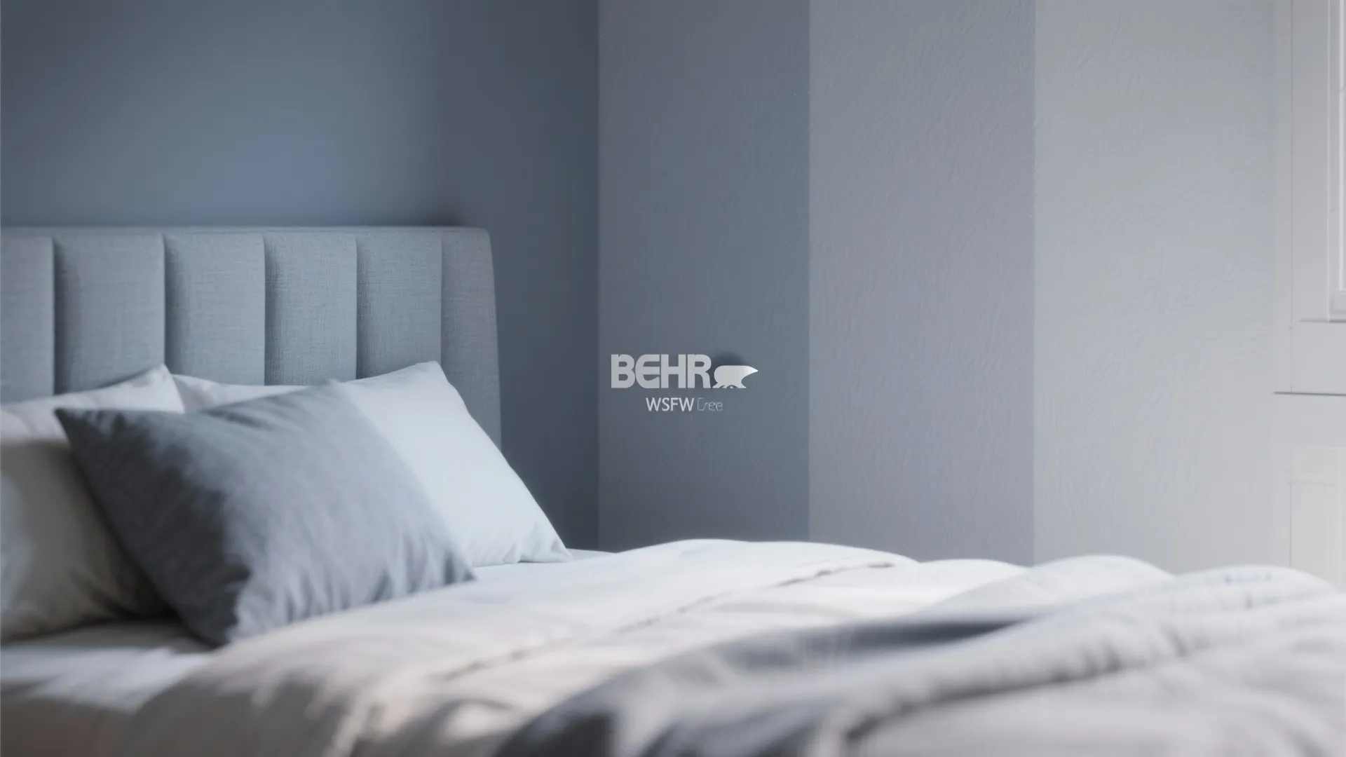 Modern bedroom with grey headboard white bedding and grey pillows next to blue painted walls