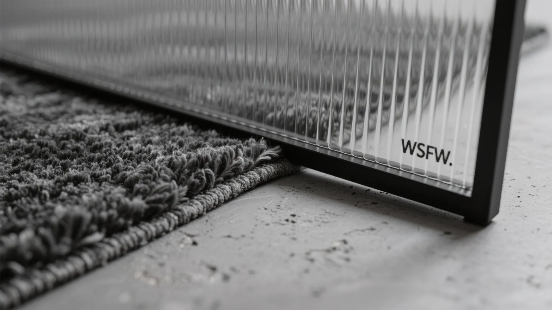 Close up view of a grey textured rug next to a ribbed glass room divider