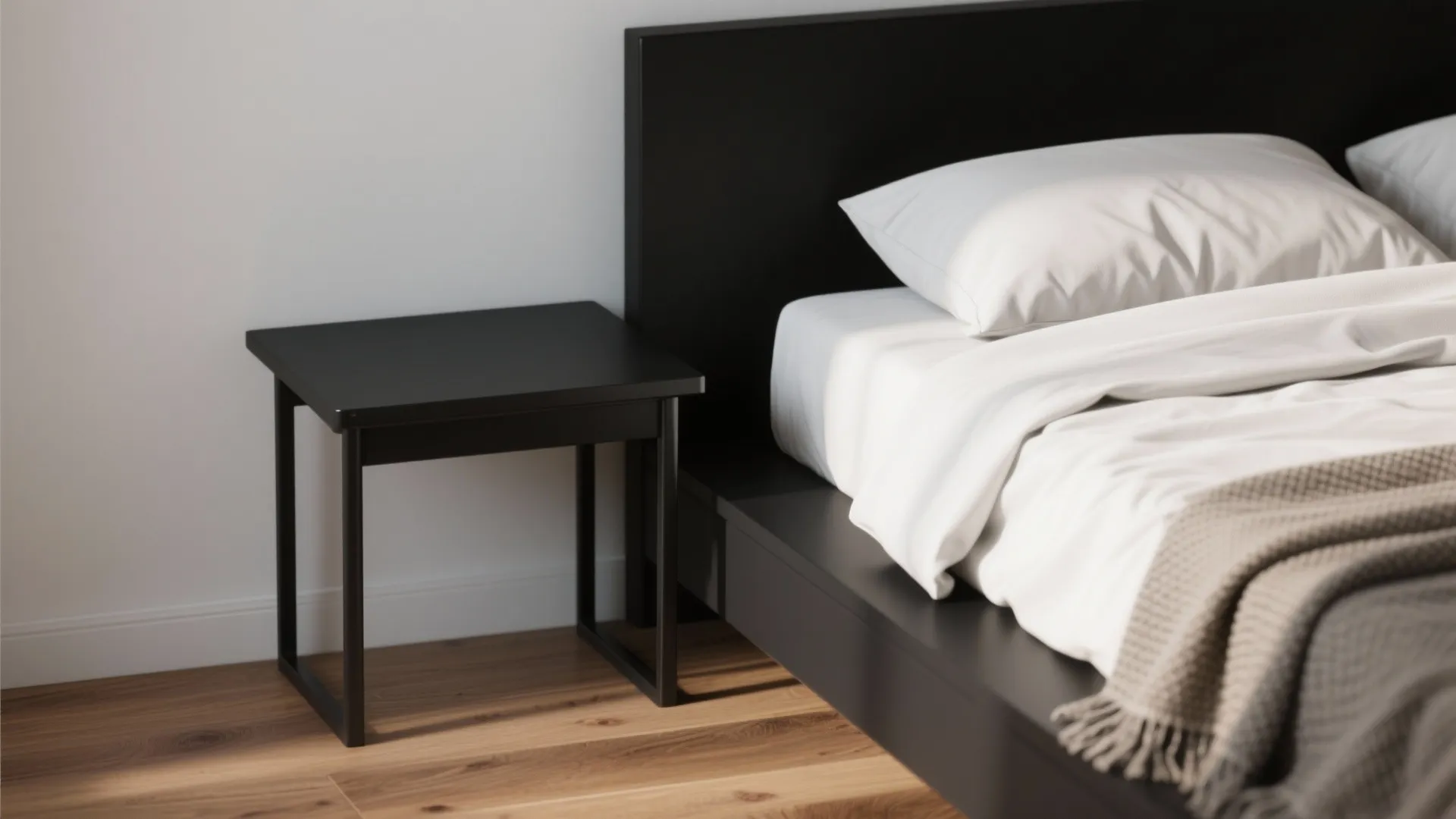 Simple black side table next to a black bed frame with white pillows on wooden floor