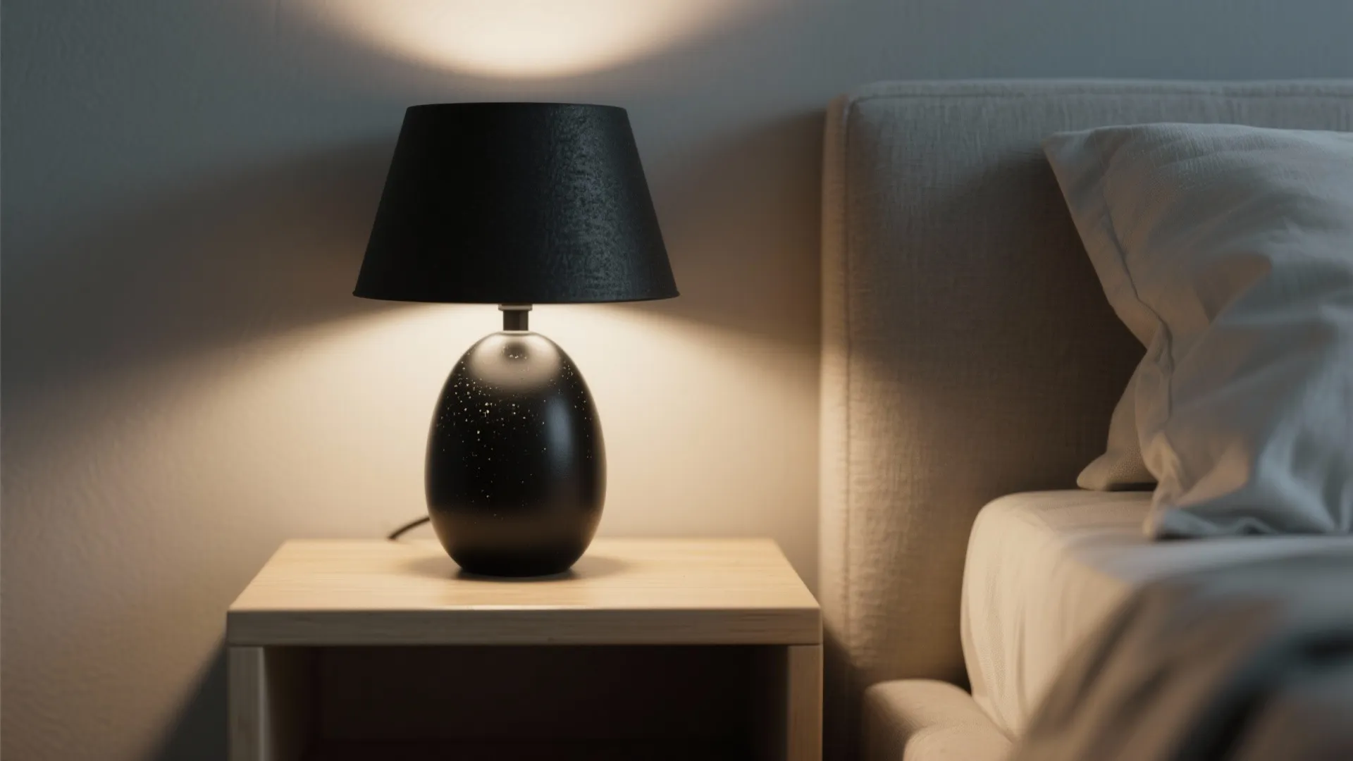 Small black table lamp on a wooden nightstand next to a bed with white pillows